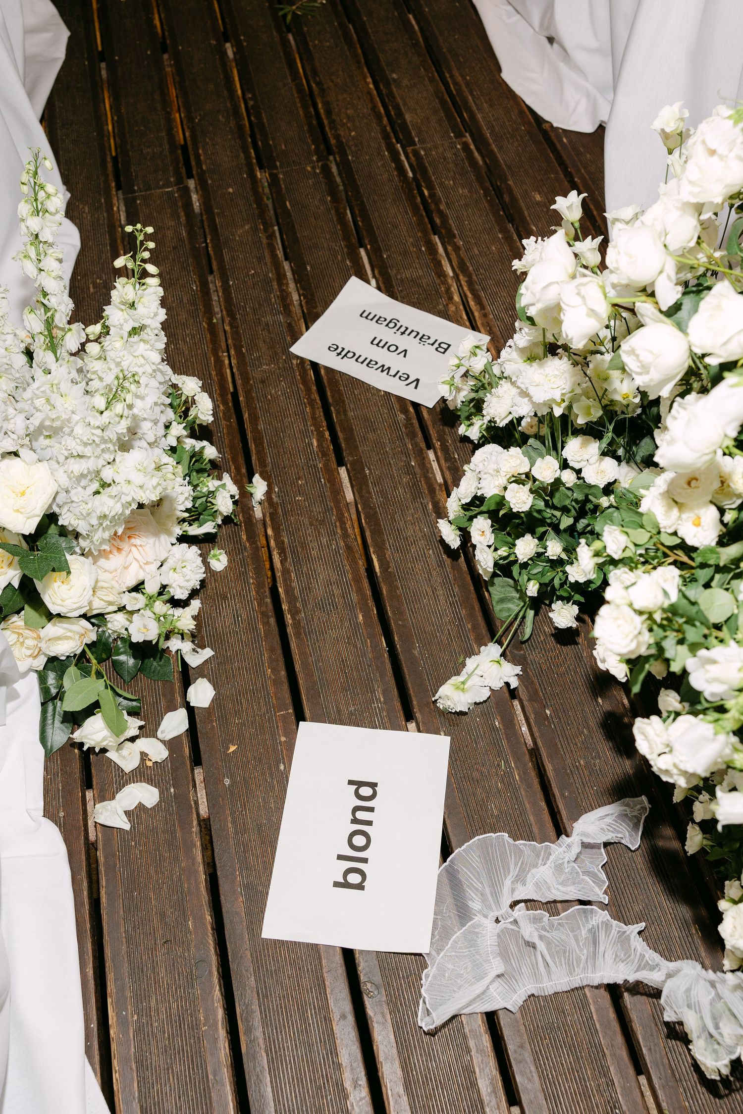 White floral arrangements and name cards displayed on dark wooden decking.