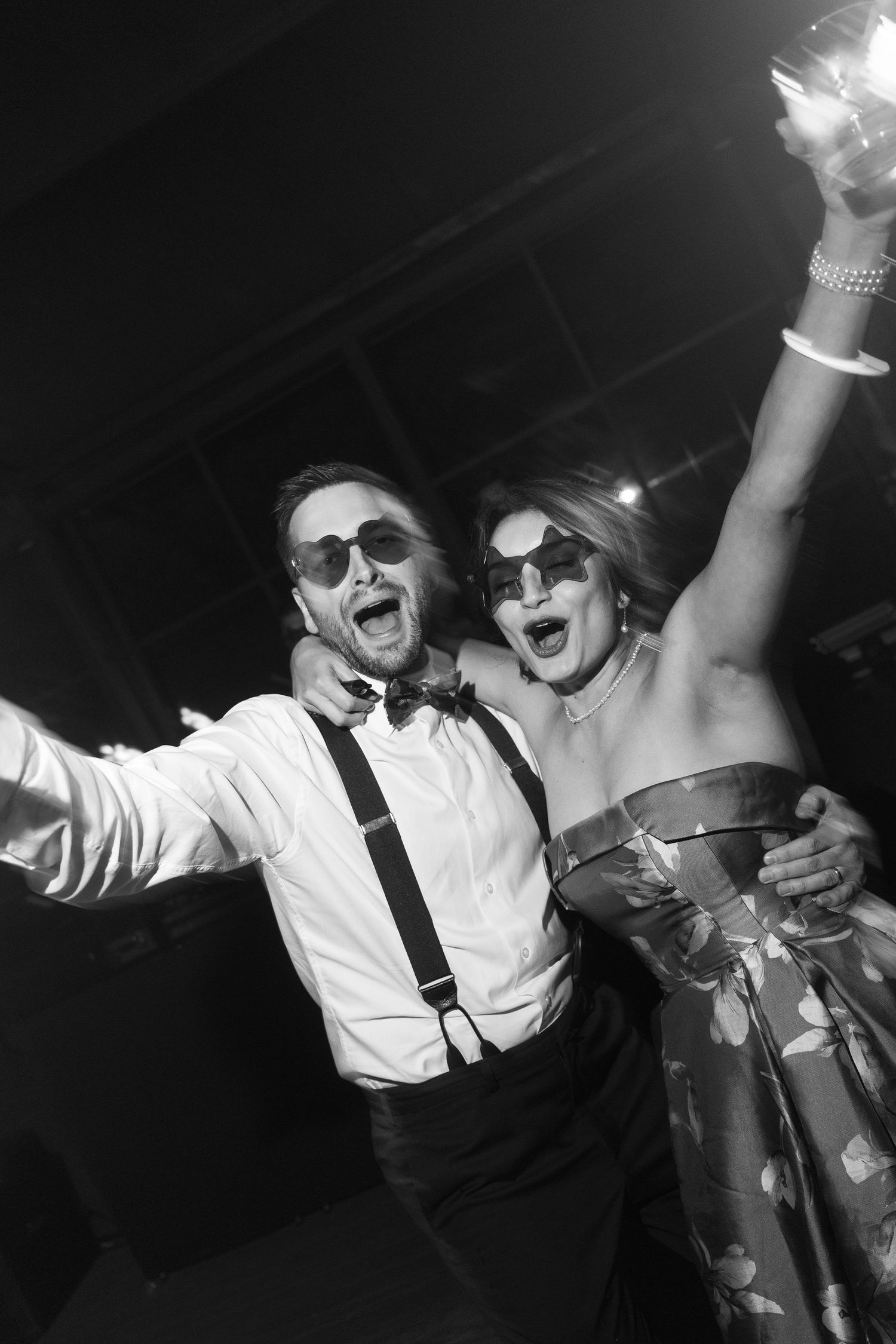 Joyful wedding guests dancing and celebrating at a reception party wearing sunglasses.