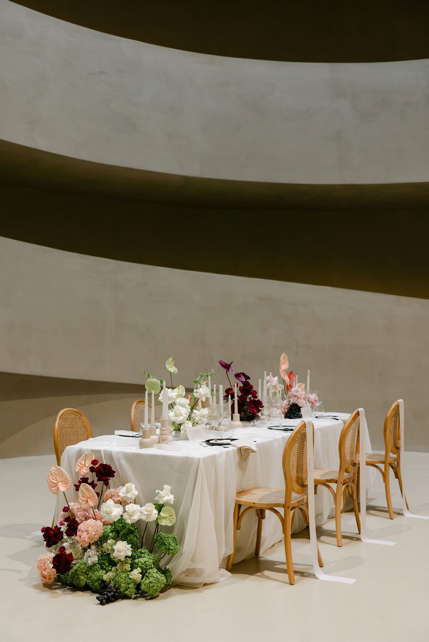 Elegant wedding reception table with floral centerpieces and candles set inside a curved modern architectural space.