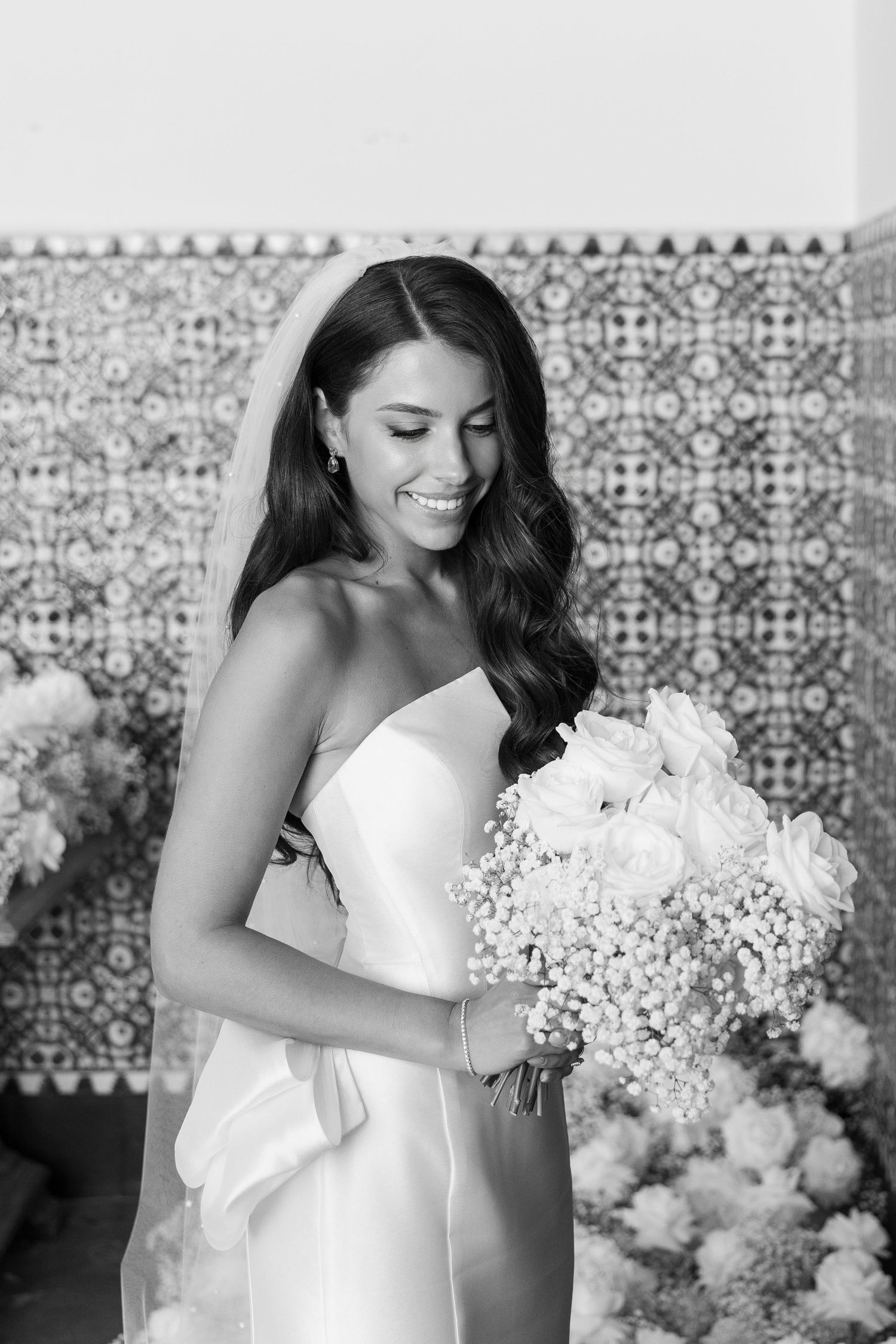 Elegant bride in white dress holding a bouquet of baby's breath flowers against a patterned tile background.
