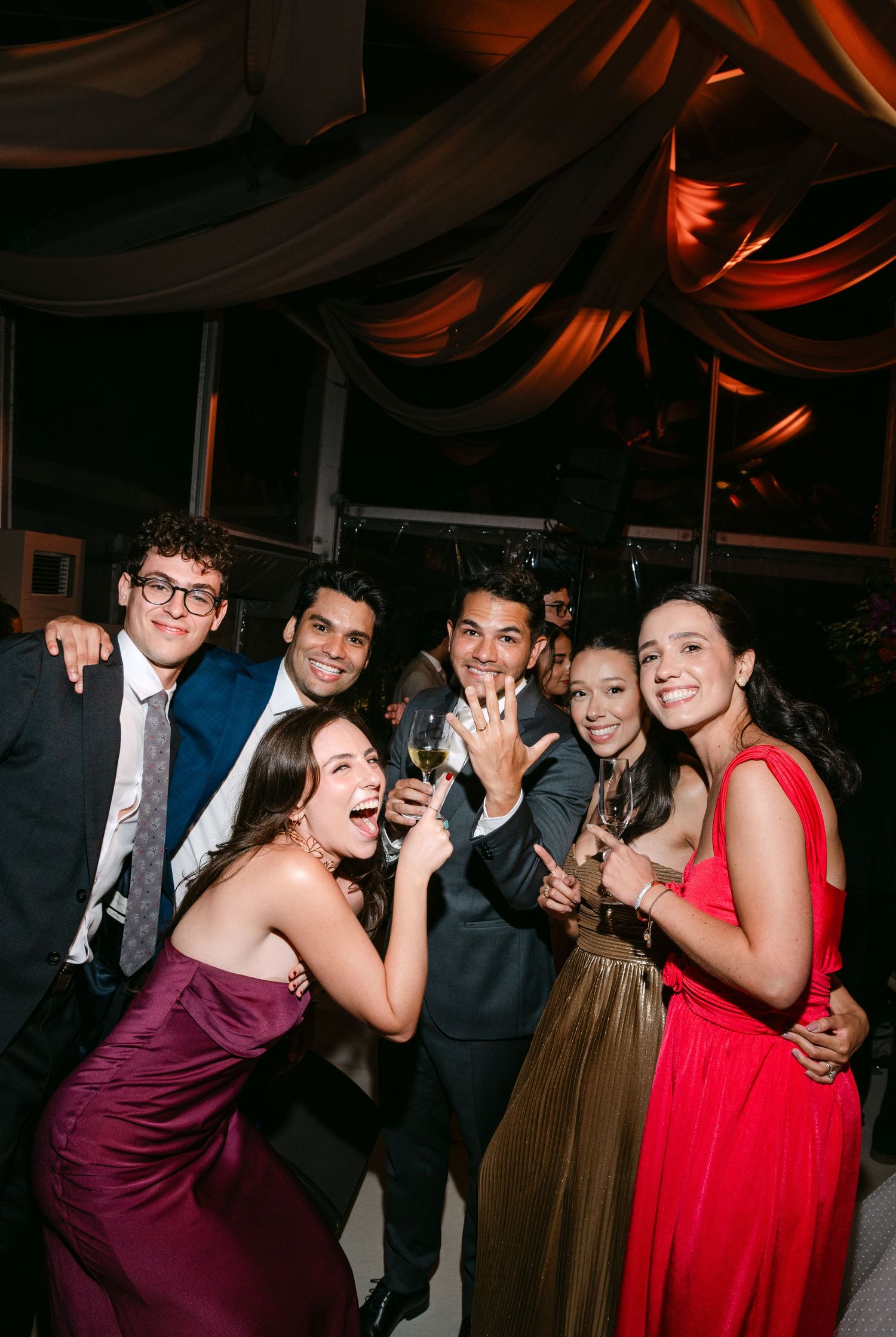 Wedding guests laughing and dancing together in colorful formal dresses at an evening reception.