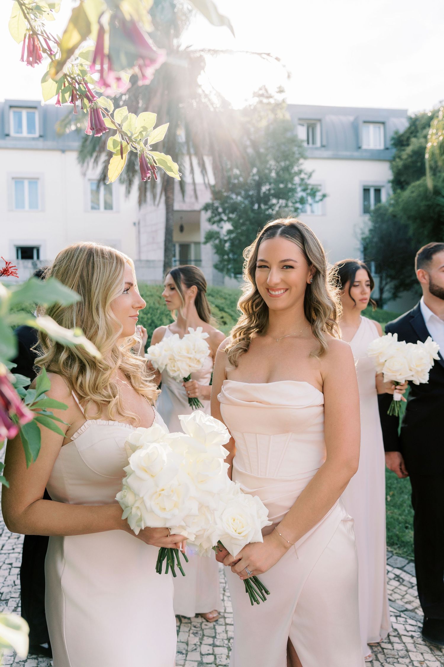 Bridesmaids in blush pink dresses holding white bouquets at an outdoor wedding ceremony.