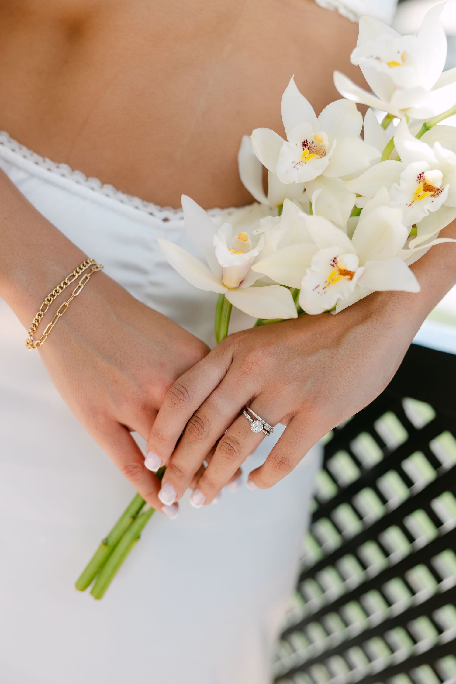 Close-up of bride's hands holding white orchid bouquet with engagement ring and bracelet visible.