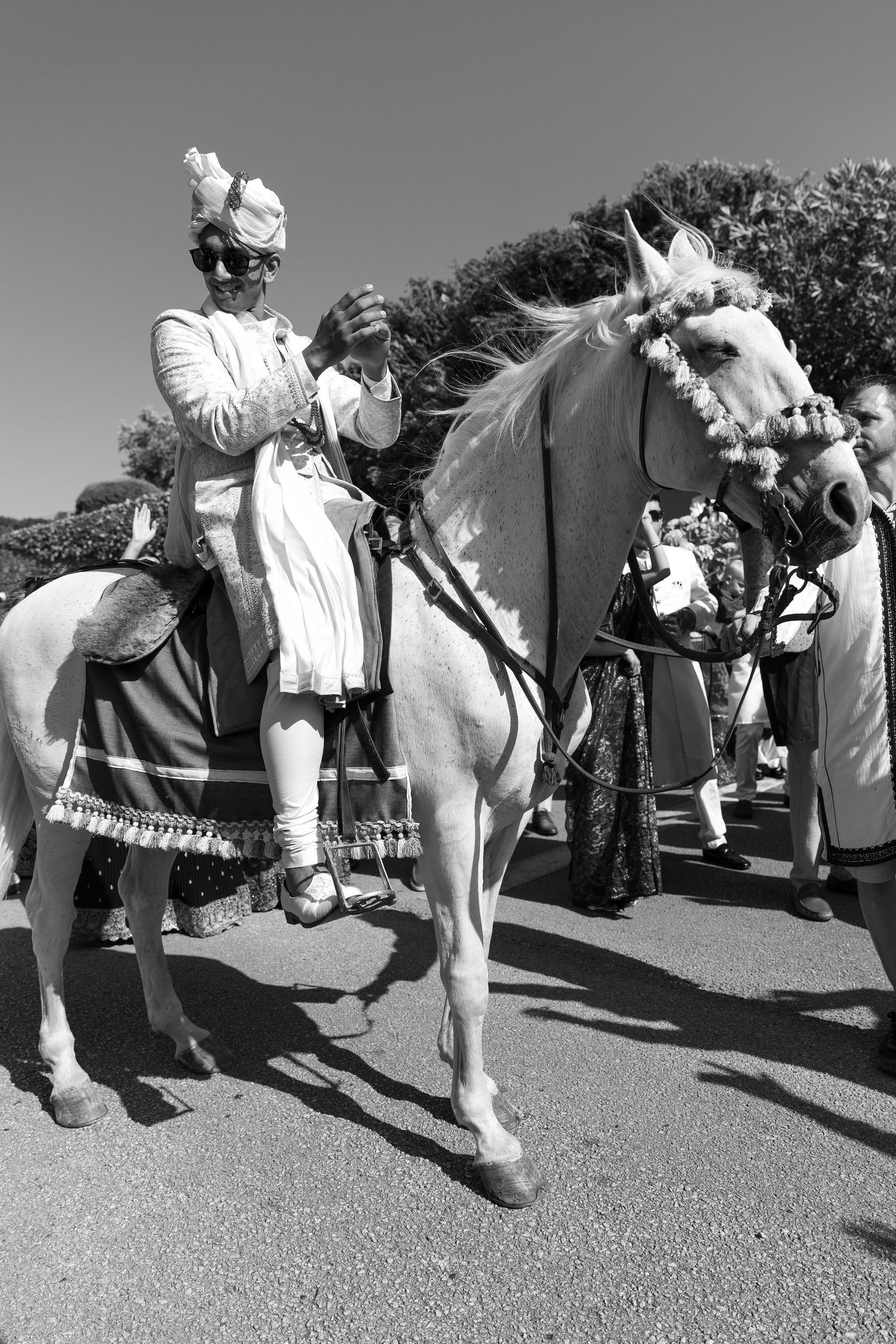 Traditional wedding procession with decorated white horse and ceremonial riders in monochrome.
