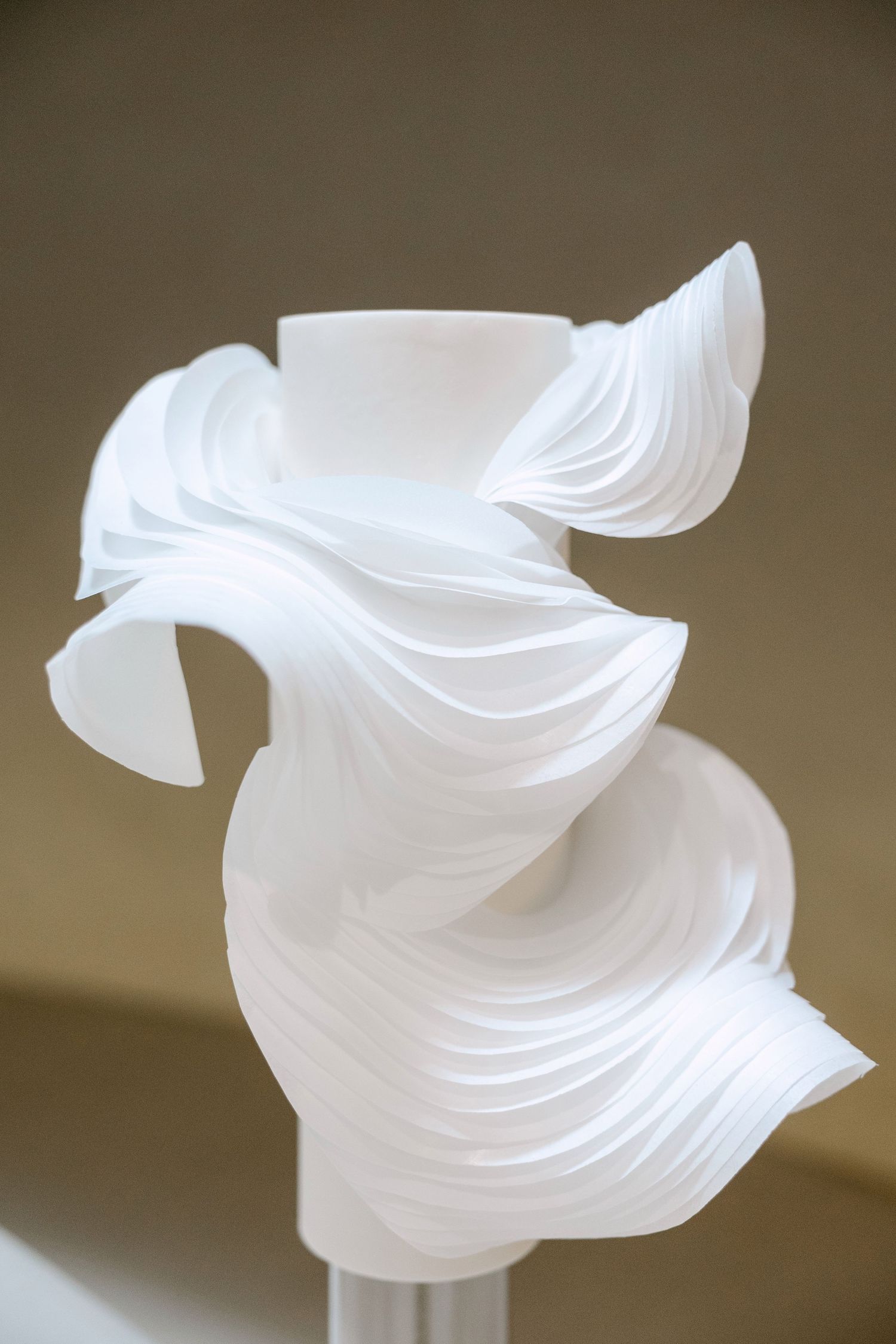 White sculptural art piece with flowing, layered curves creating an elegant twisted form against a neutral background.