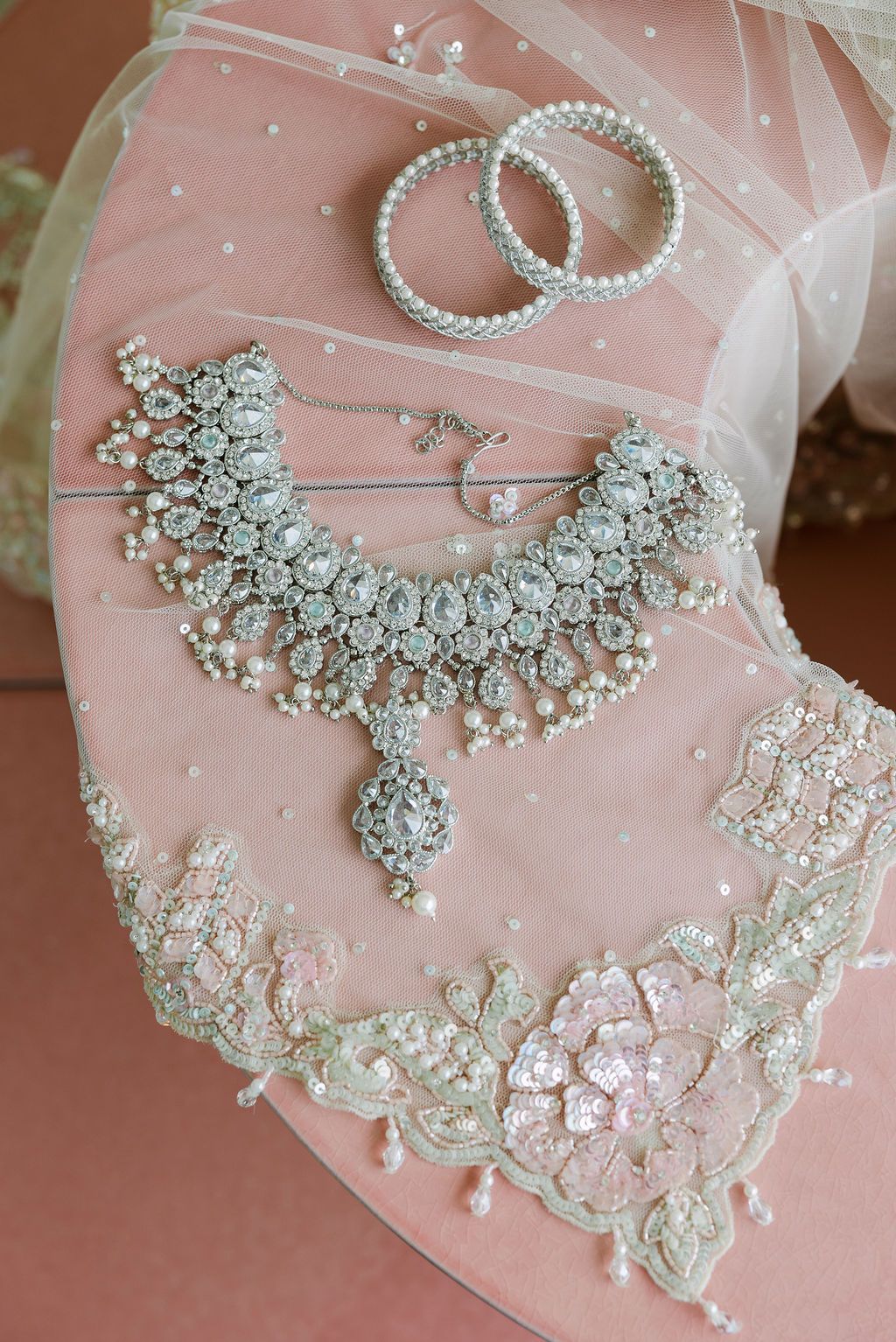 Elegant bridal jewelry including crystal necklaces and accessories displayed on pink silk fabric.
