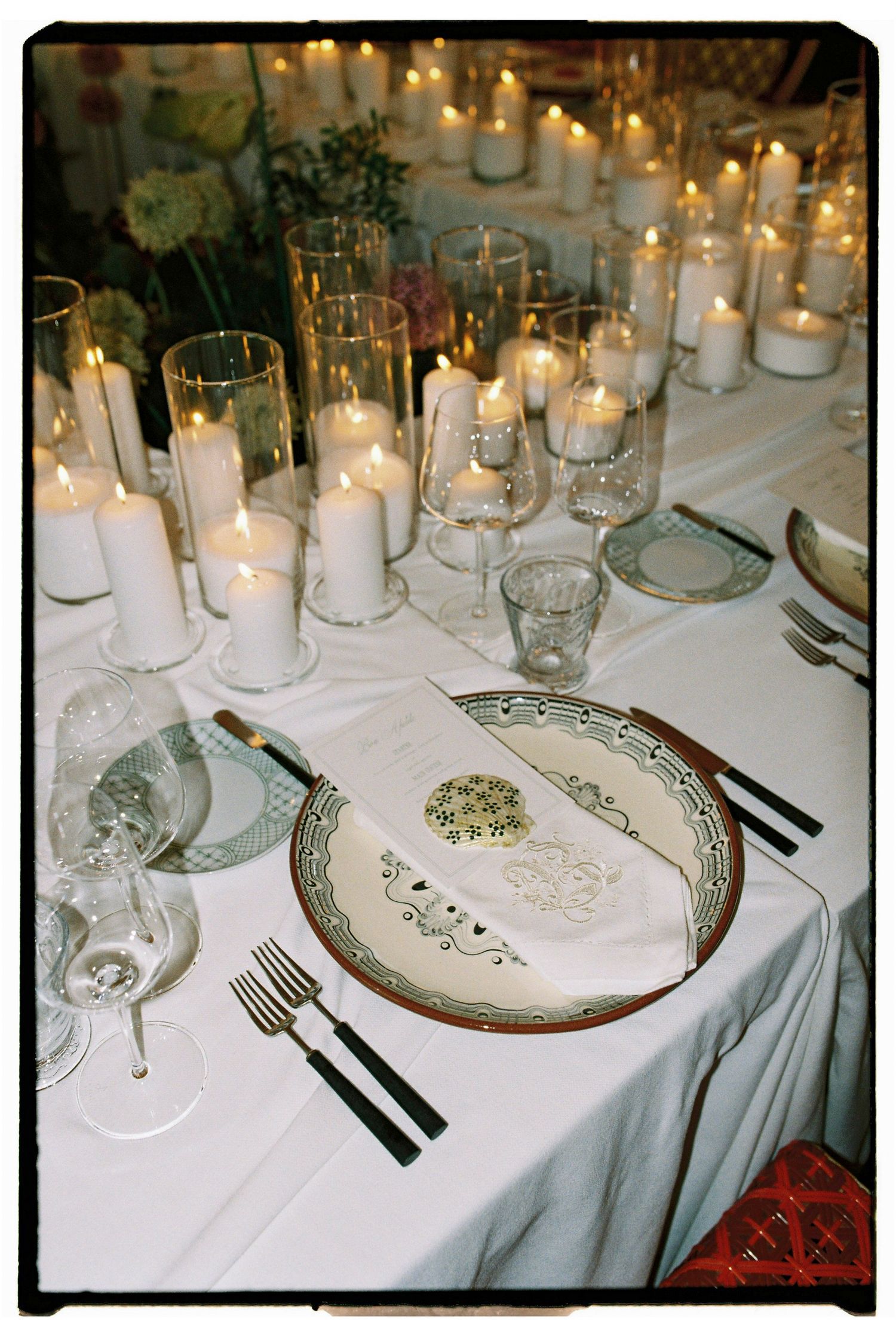 Elegant candlelit table setting with white pillar candles, crystal glasses, and decorative plate with folded napkin.