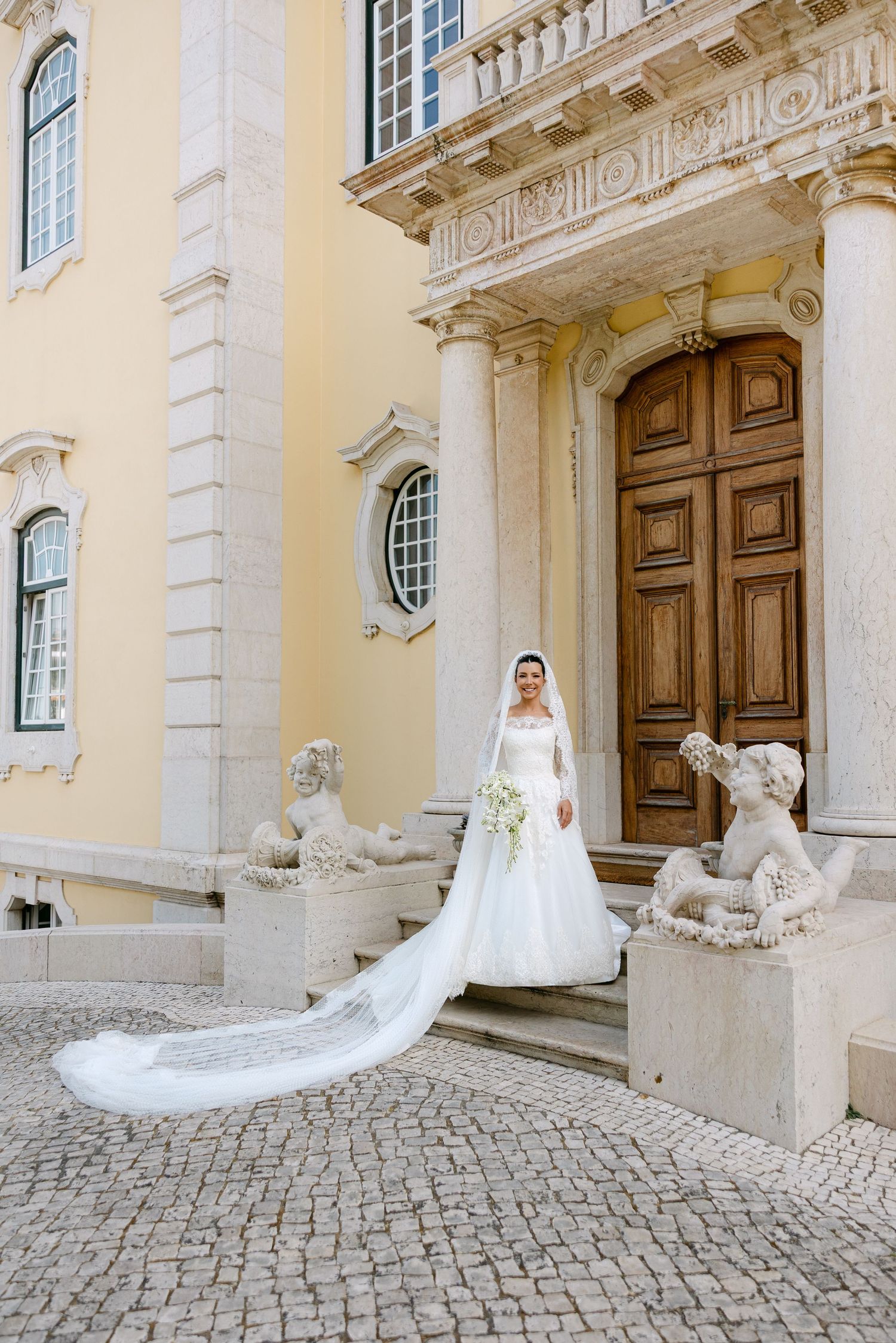 A stunning wedding dress photo at a historic building entrance with stone lions and cobblestone path.