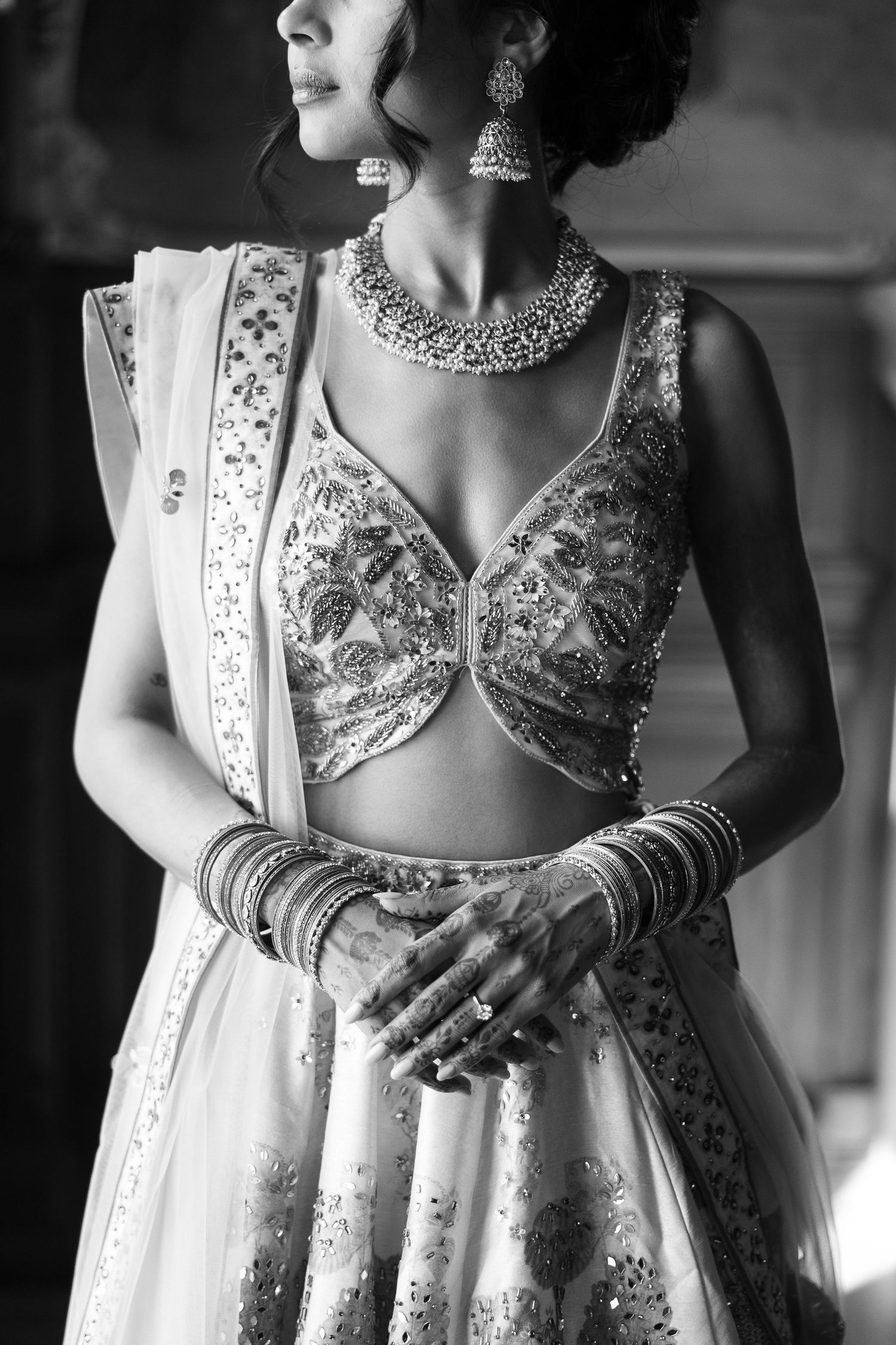 Elegant Indian bridal attire with intricate embellishments and traditional jewelry in black and white.