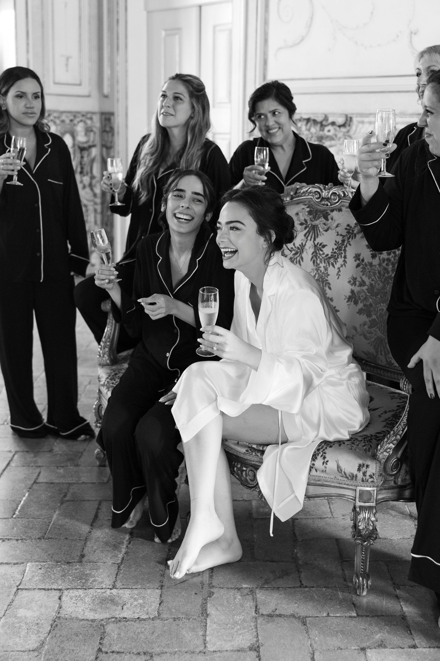 Group gathered in an ornate room sharing champagne and laughter during wedding preparations.
