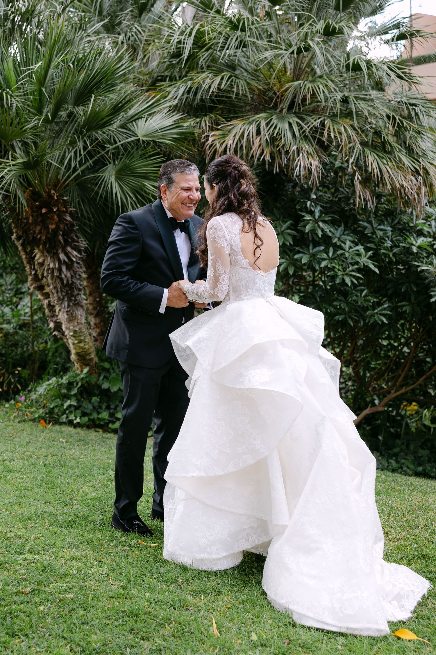Couple dances joyfully among palm trees in a garden setting.