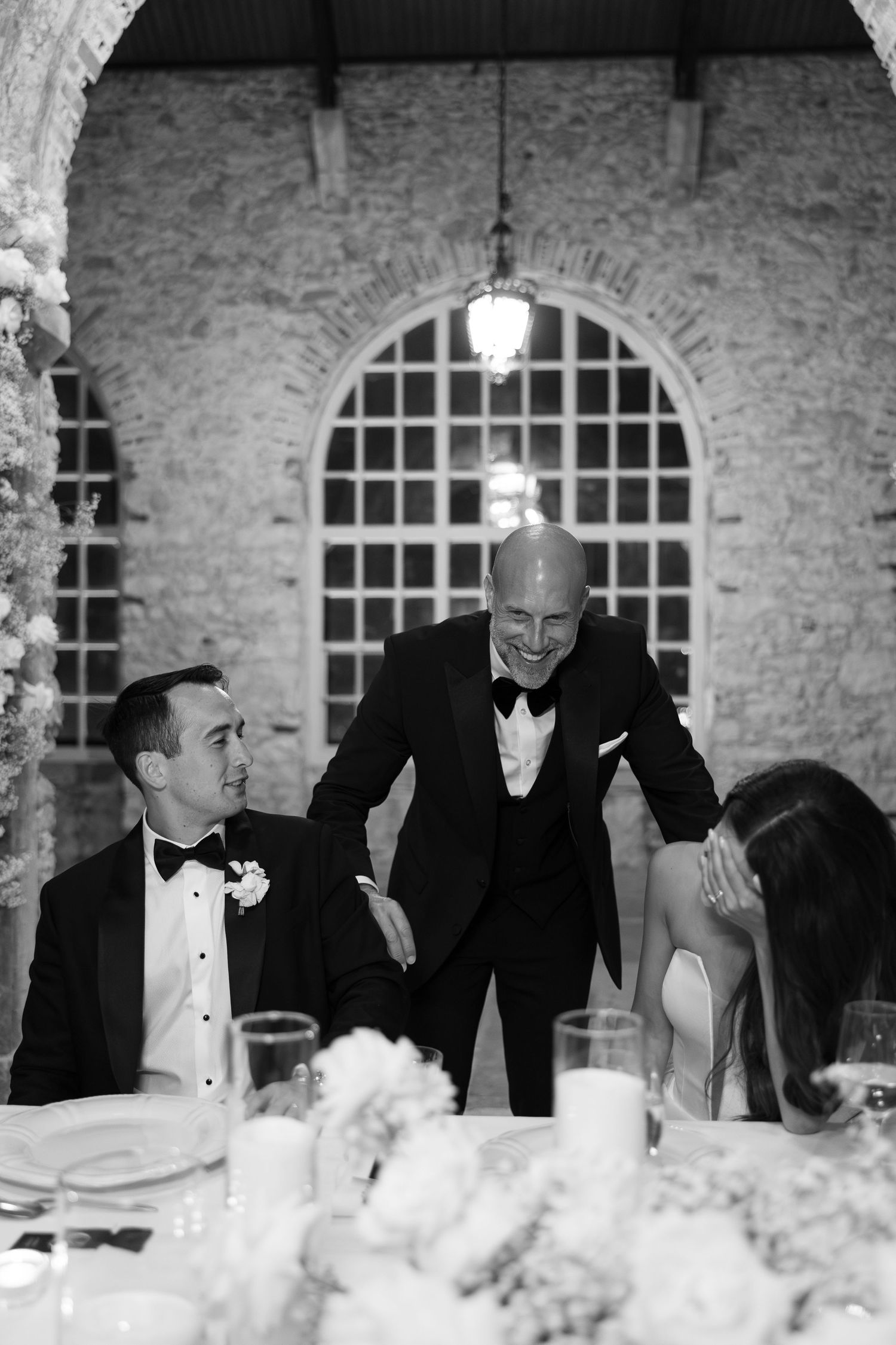 Wedding reception scene in a rustic stone venue with arched windows.