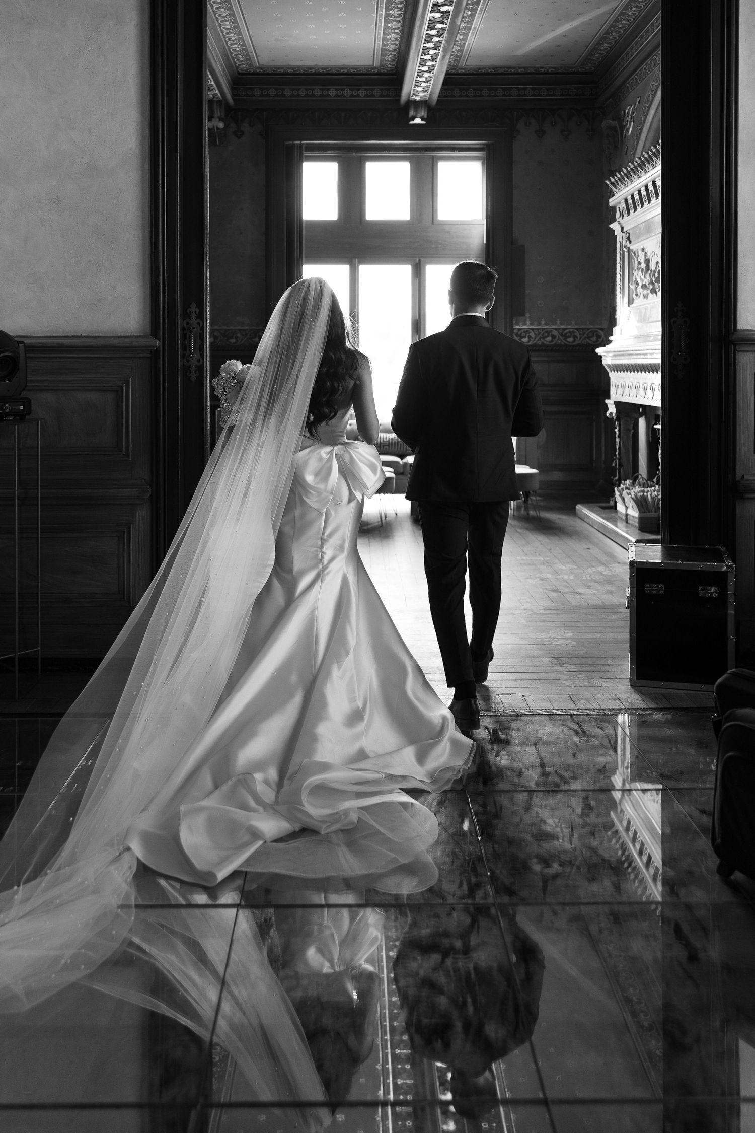 Dramatic black and white photos of couple walking through a grand hallway with reflective floors.
