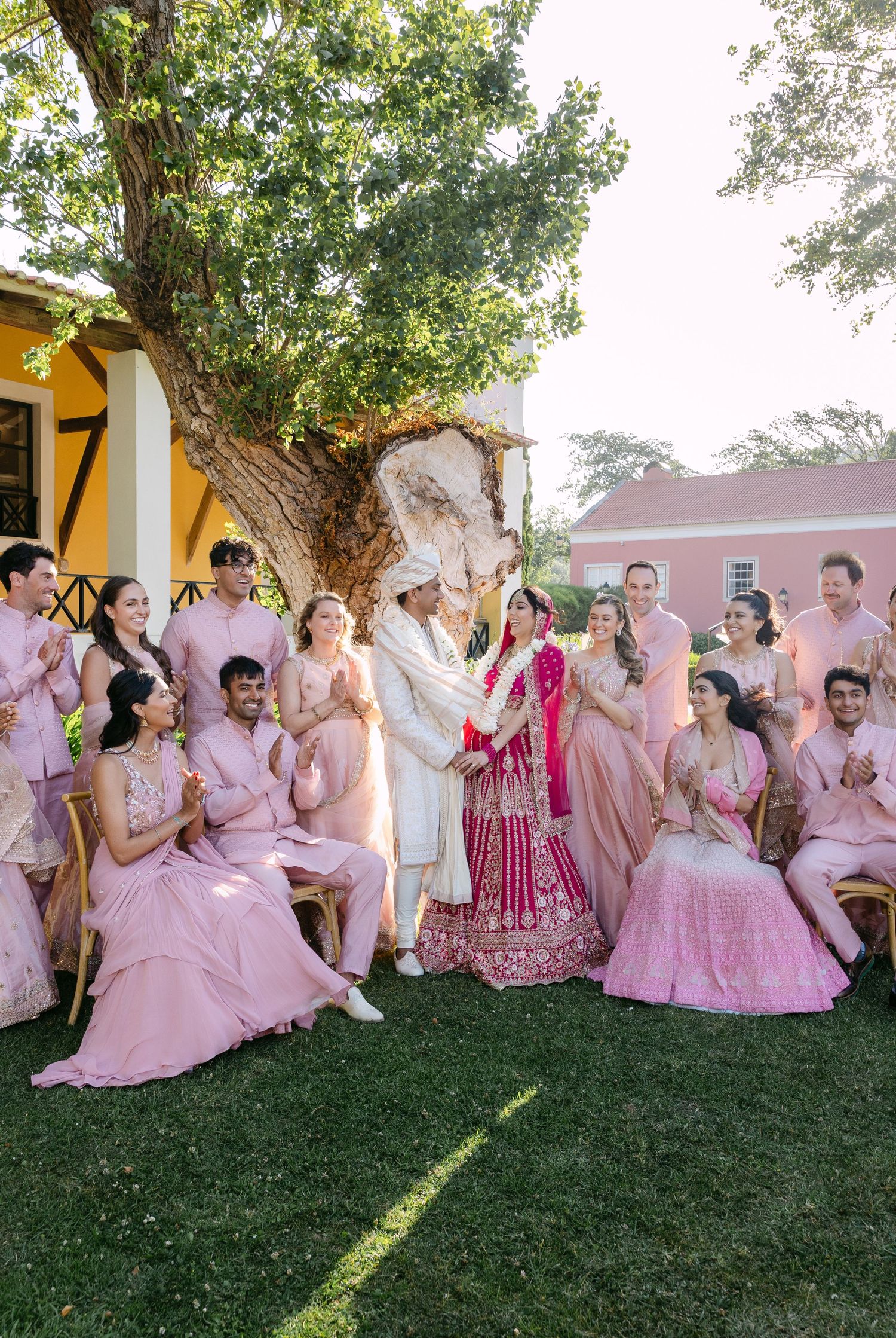 Large wedding party wearing pink and white outfits gathered outdoors for group photos.