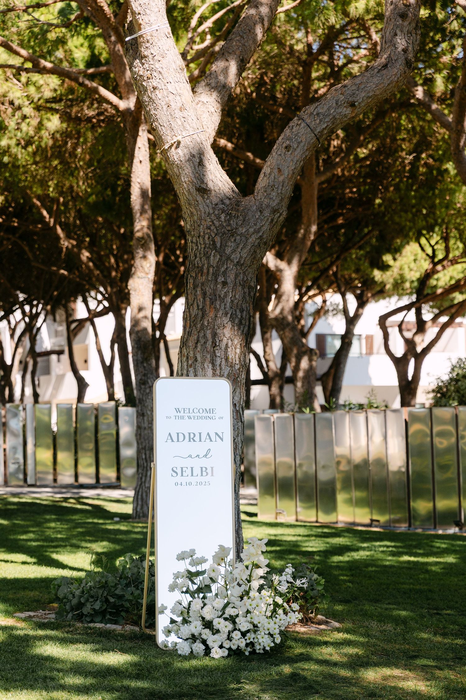 Wedding welcome signs decorated with white flowers displayed among trees in a garden setting.