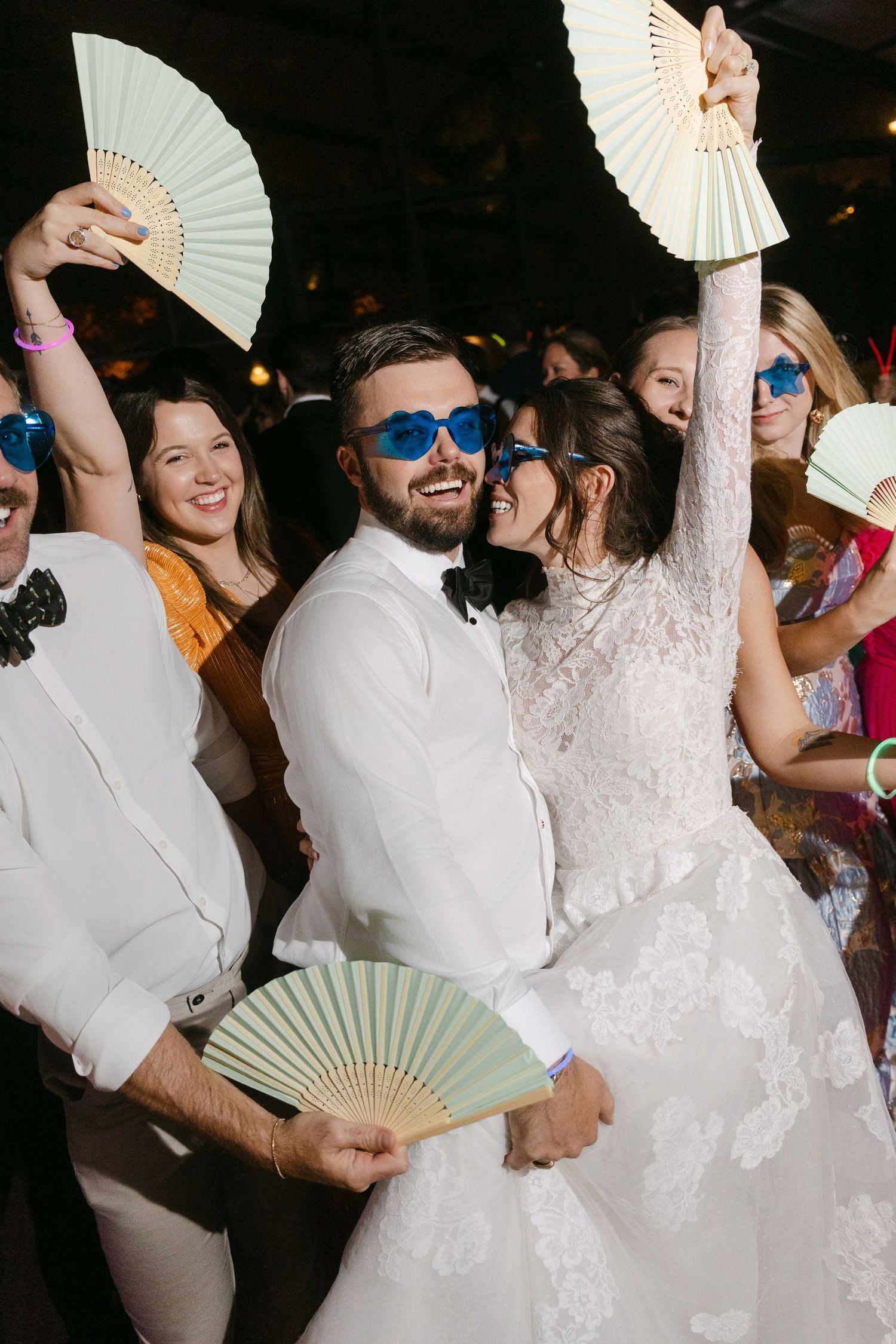 Wedding celebration with guests holding decorative white paper fans on the dance floor.