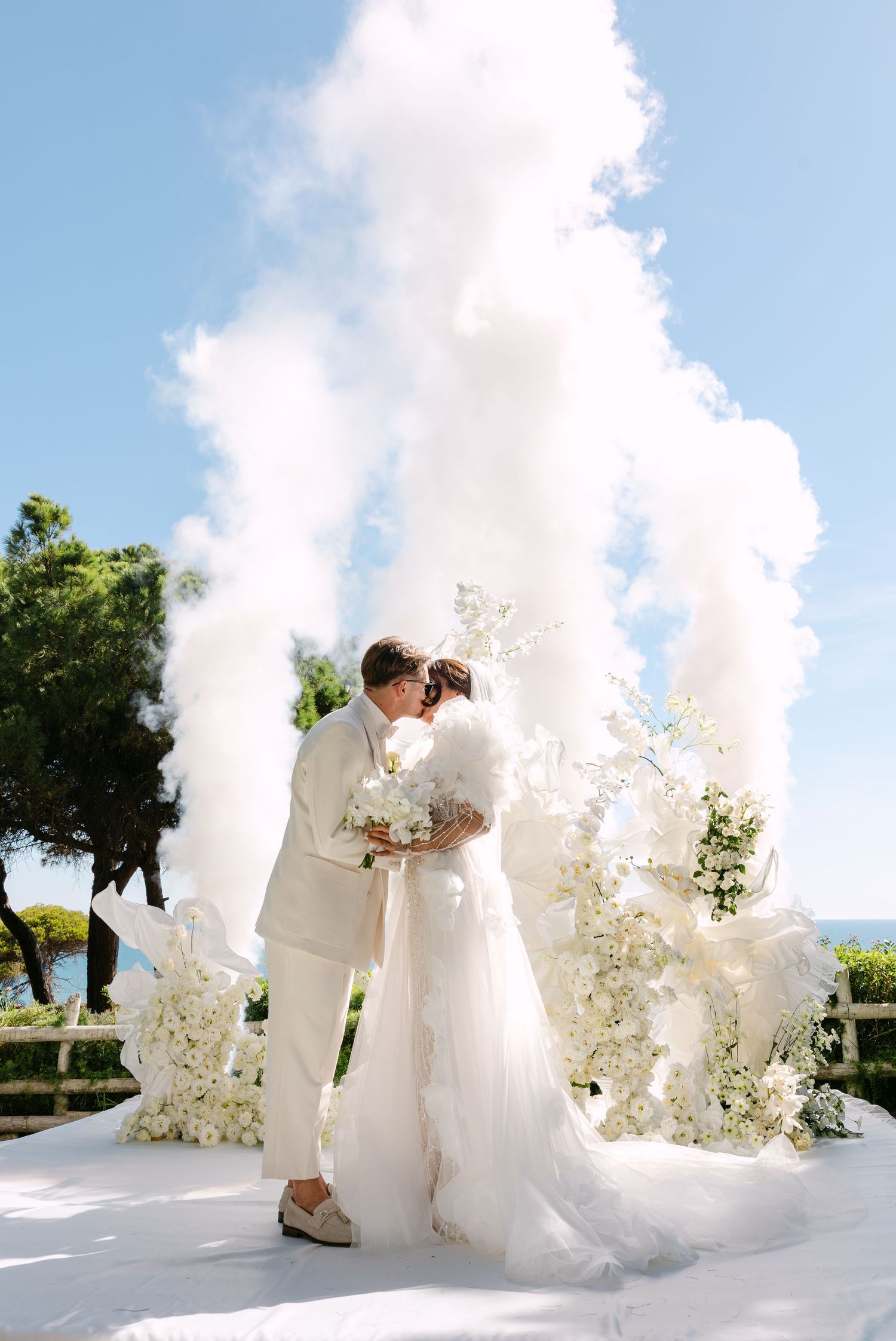Wedding ceremony setup with white floral arrangements against a bright blue sky.