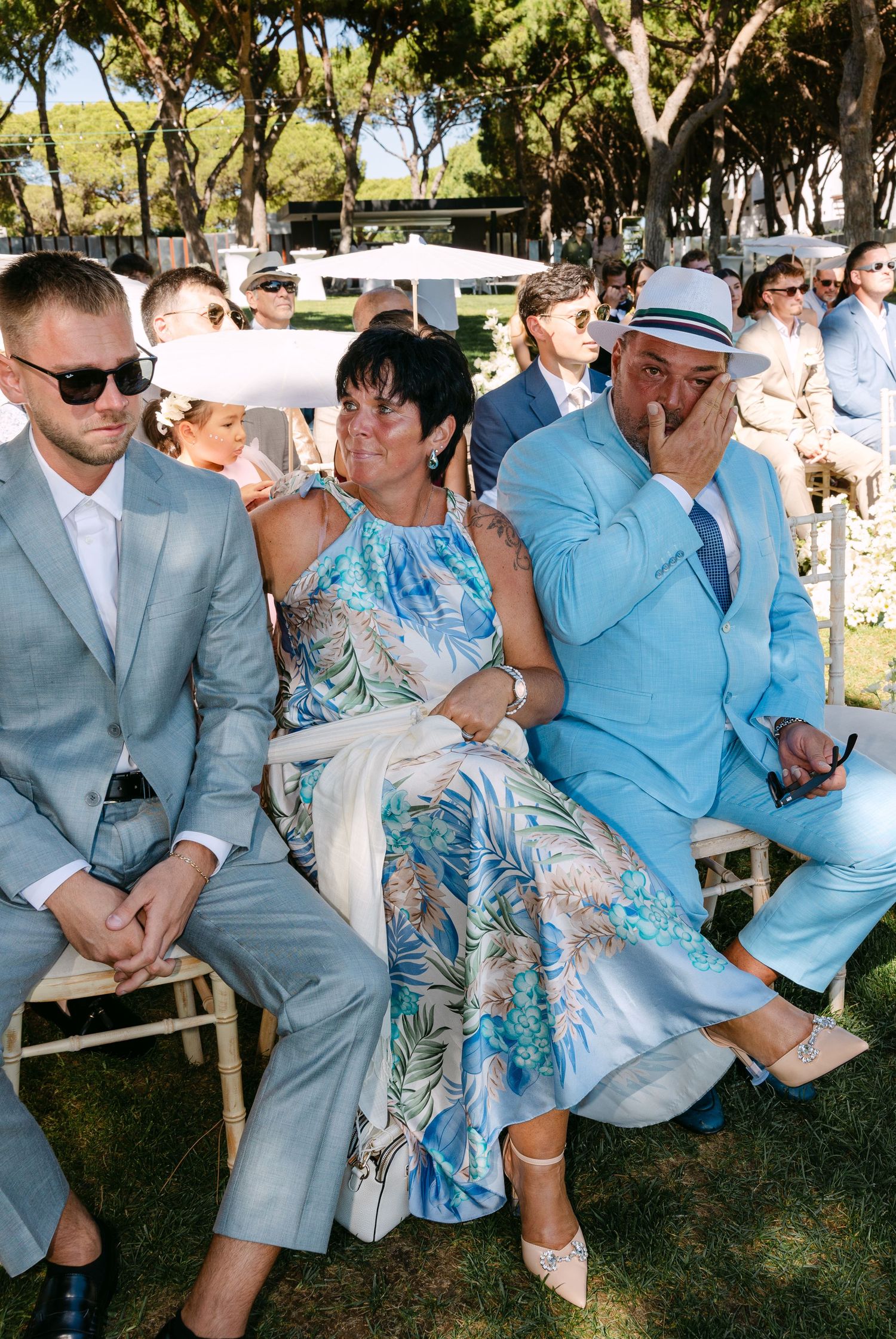 Wedding guests in light blue and gray suits relaxing on outdoor benches.