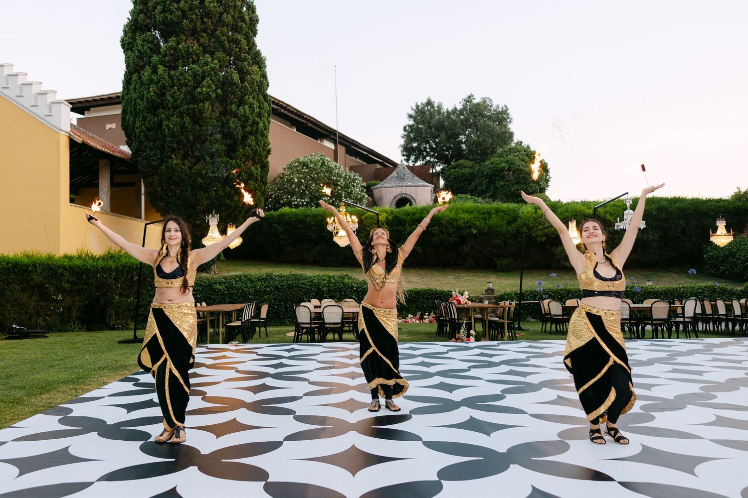 Dancers perform on black and white checkered outdoor dance floor at dusk.