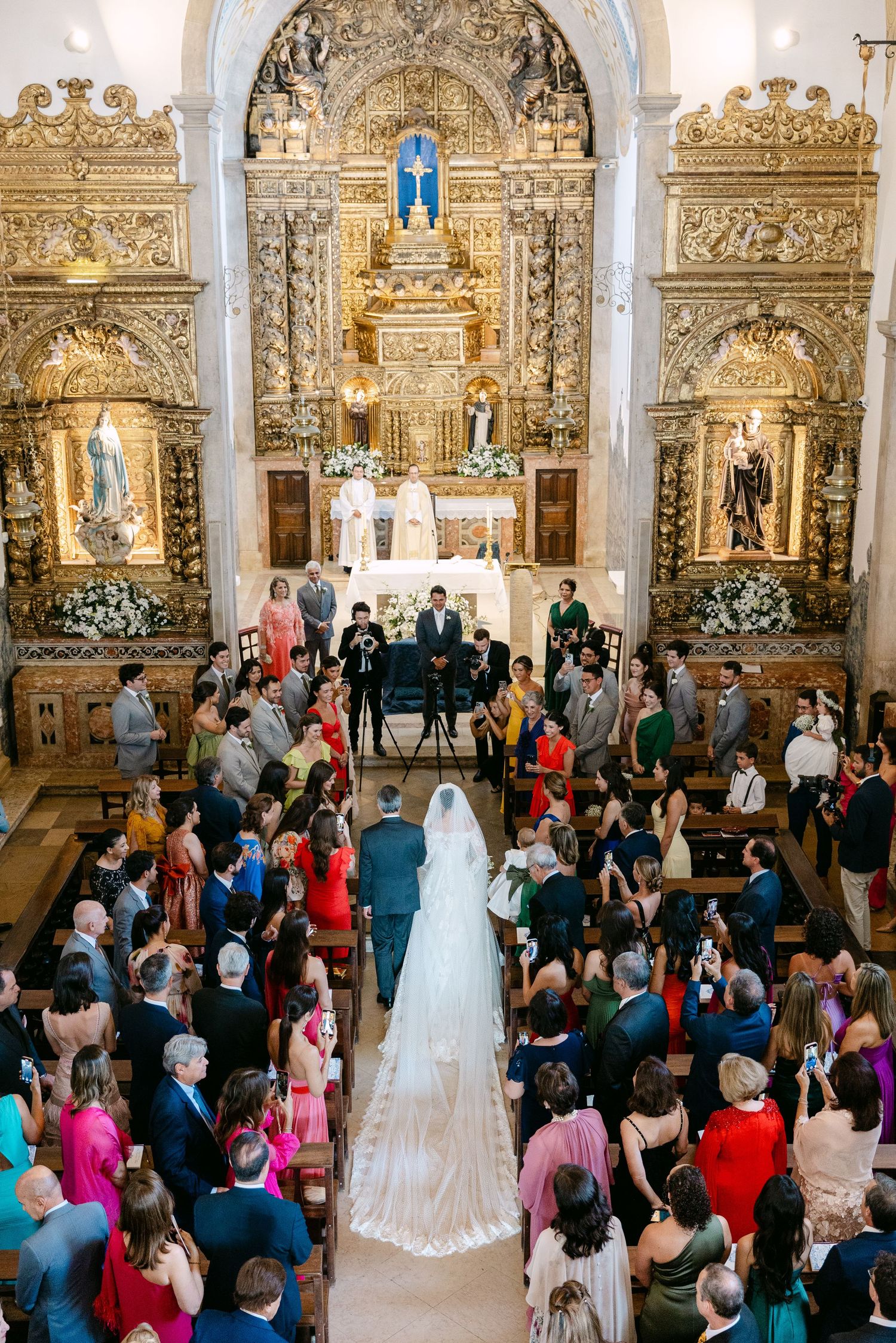 Aerial view of a wedding ceremony in an ornate church filled with colorfully dressed guests.