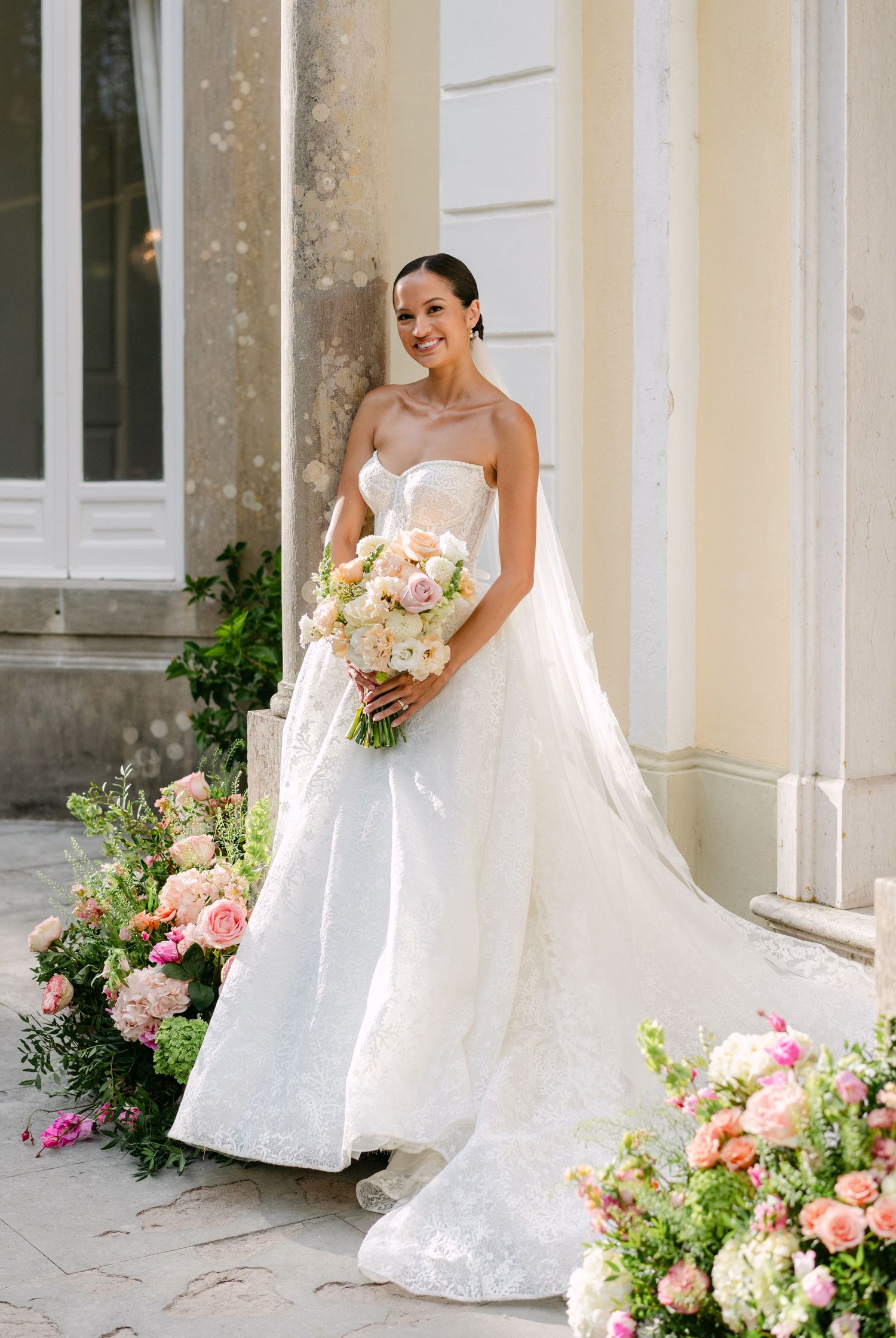 Elegant bridal portraits against a classic cream building with pink floral accents.