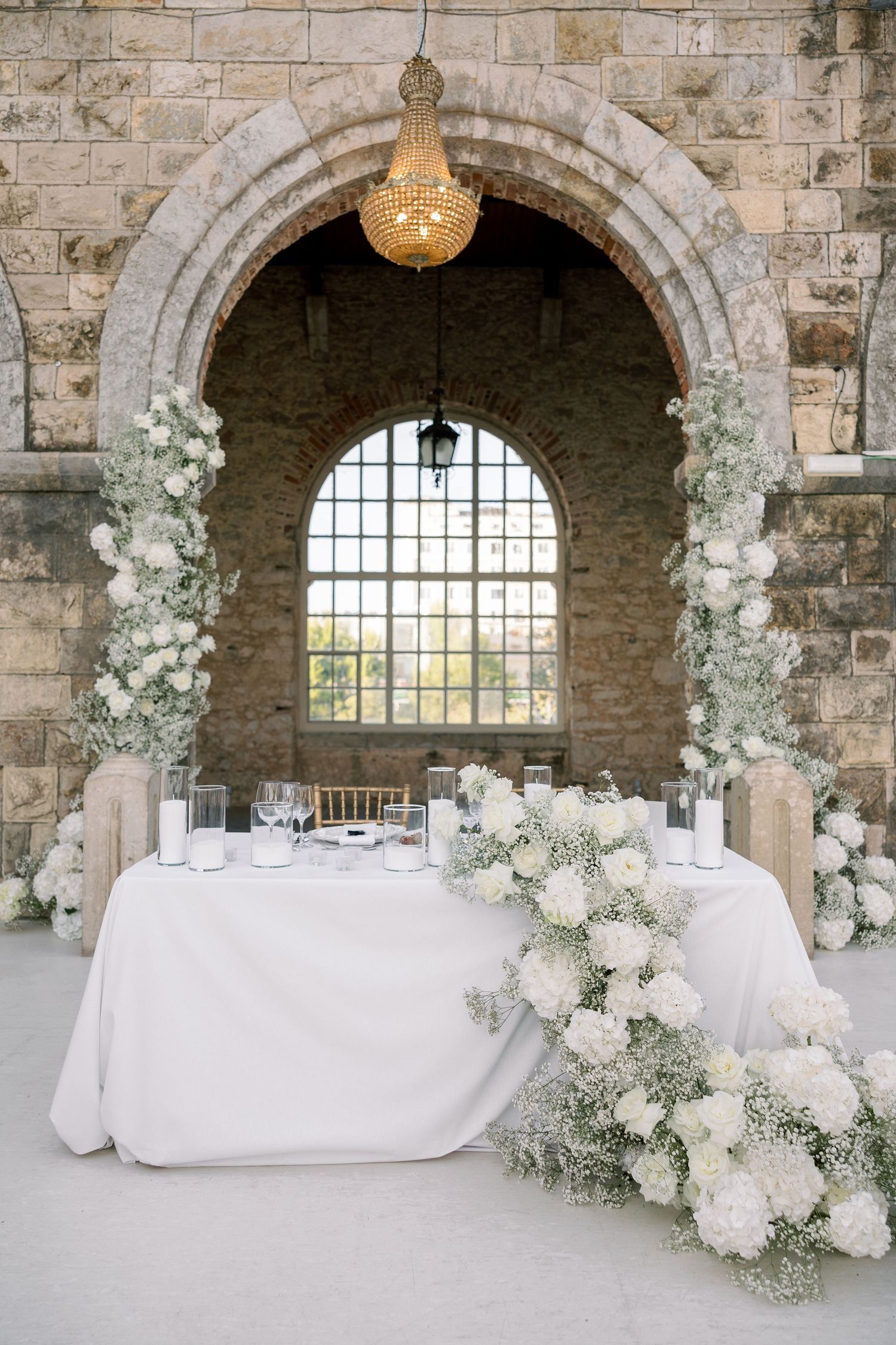 White wedding reception setup with floral arrangements in stone castle archways.