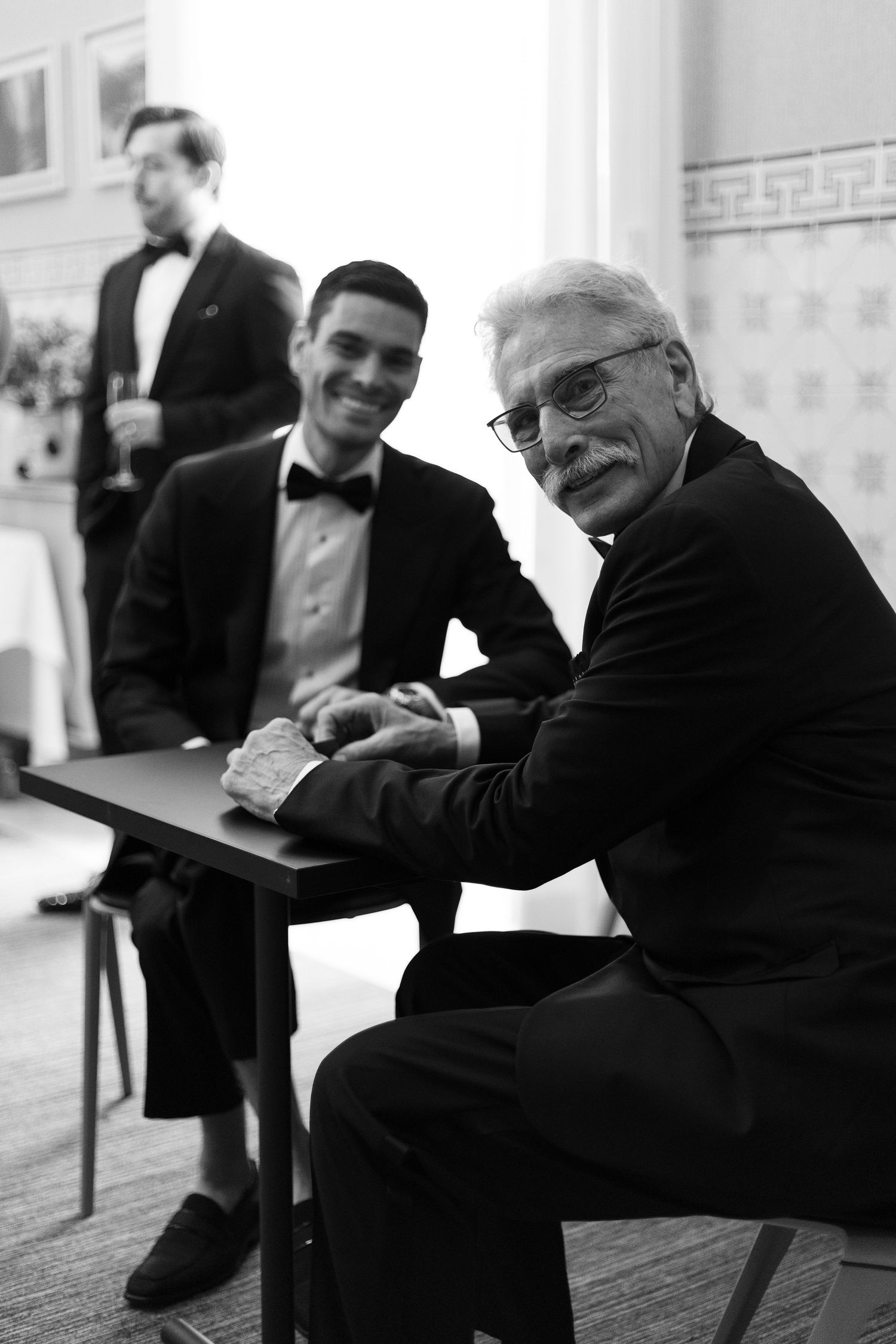 Group of formally dressed people sharing candid moments in black and white.