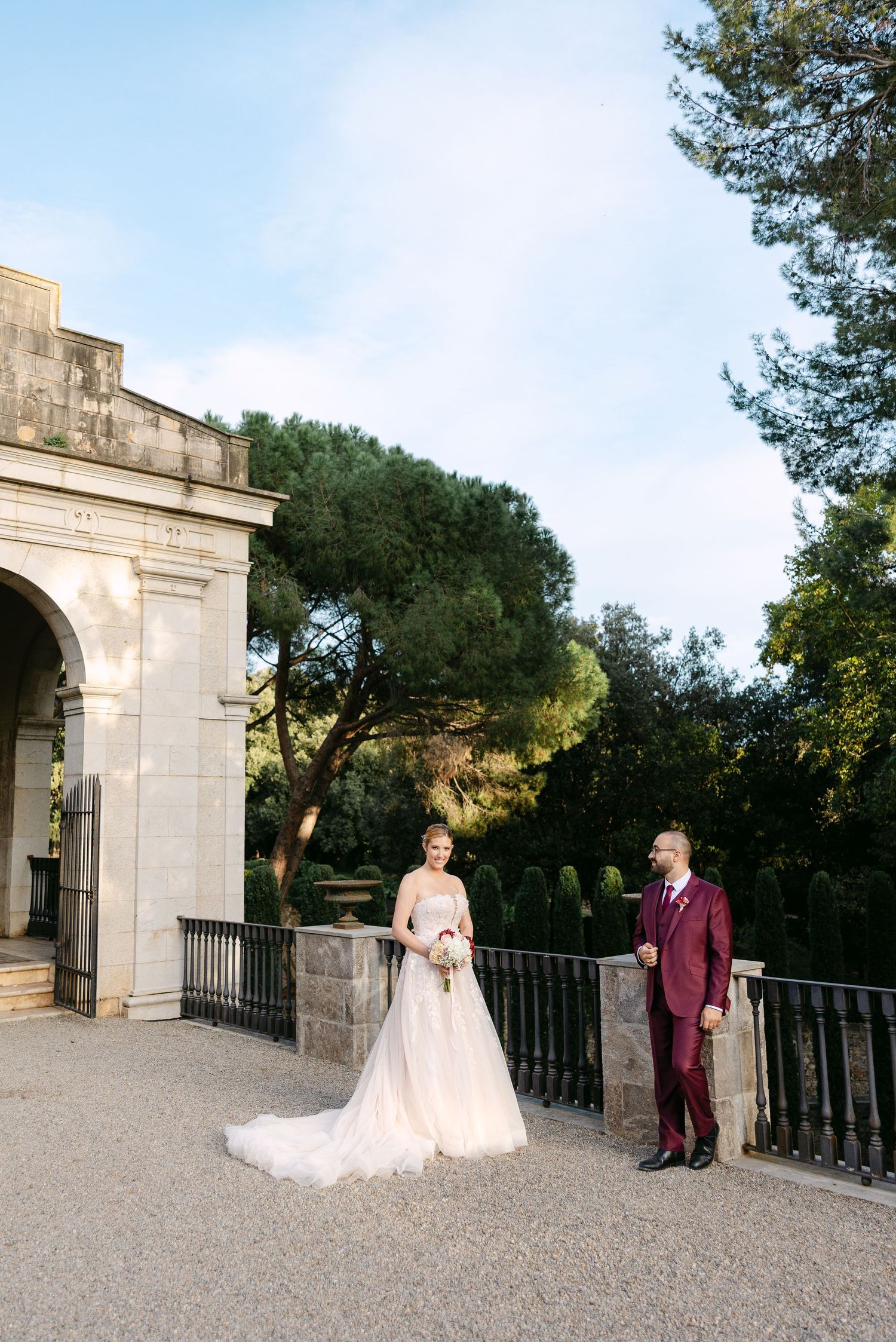 Wedding couple poses at an elegant stone archway entrance during golden hour.