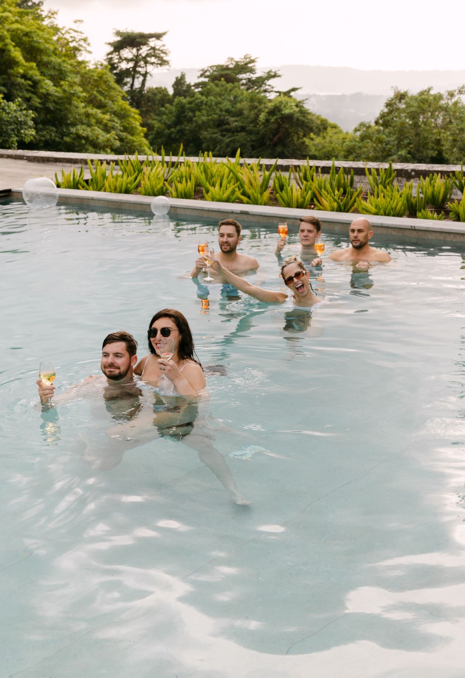 Wedding guests enjoying drinks while relaxing in an infinity pool with mountain views.