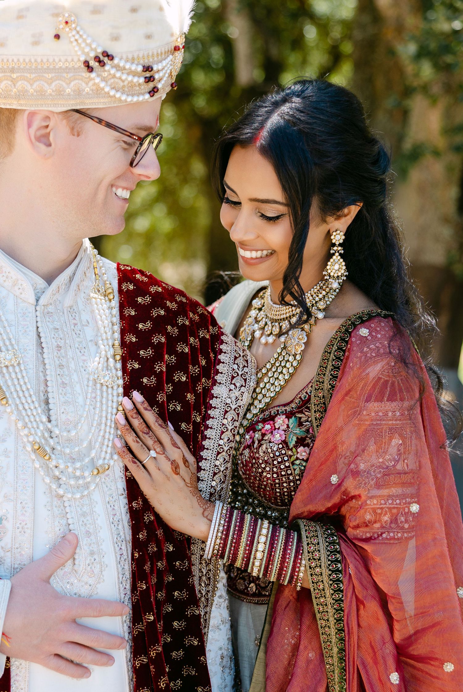A couple walking together in fusion wedding attire along a tree-lined path.