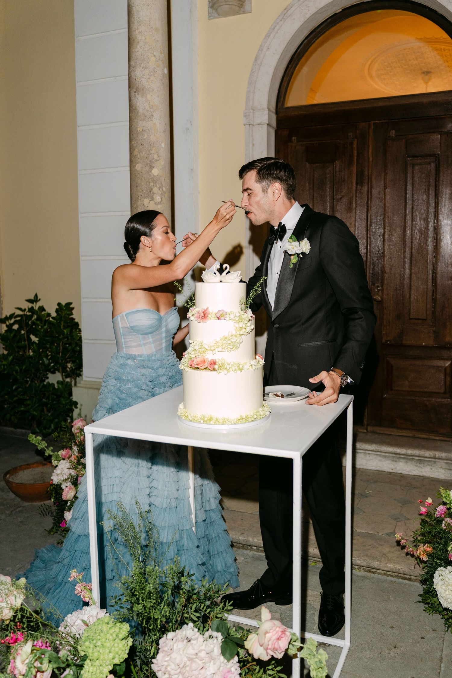 Couple shares playful moment while cutting their elegant white wedding cake.