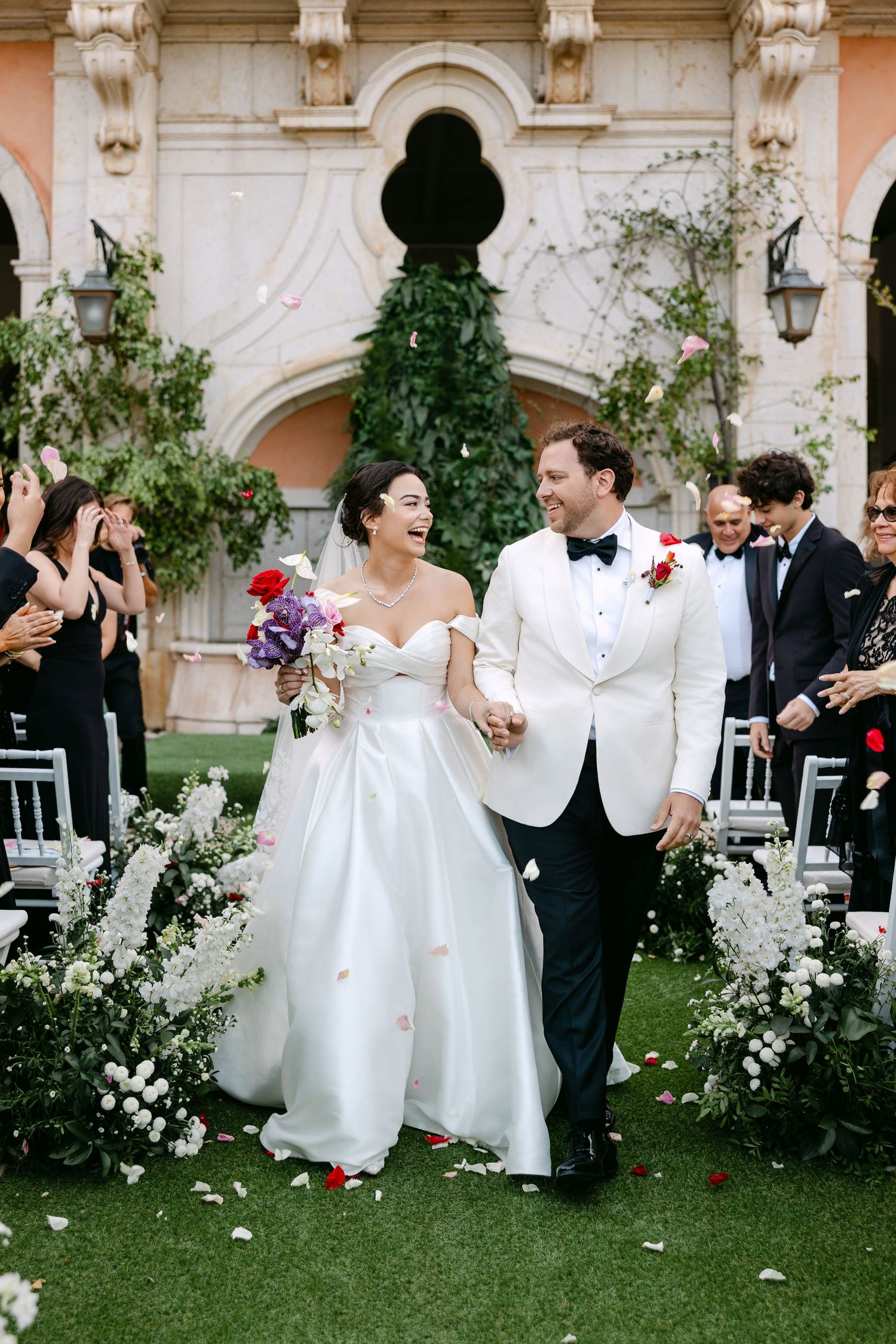 Wedding celebration with guests throwing flower petals on a beautiful lawn with classical architecture.