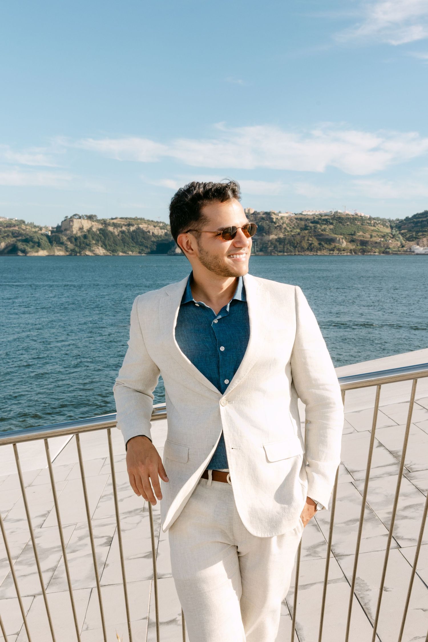 Scenic waterfront photoshoot with white suit and navy shirt against ocean backdrop.