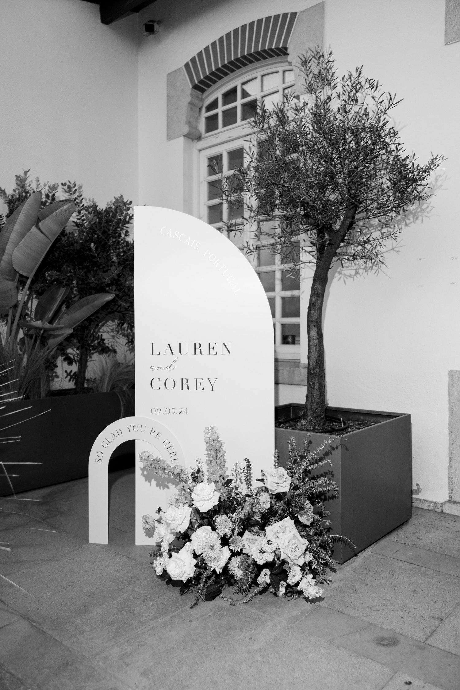 Modern wedding venue entrance with white floral arrangements and signage.