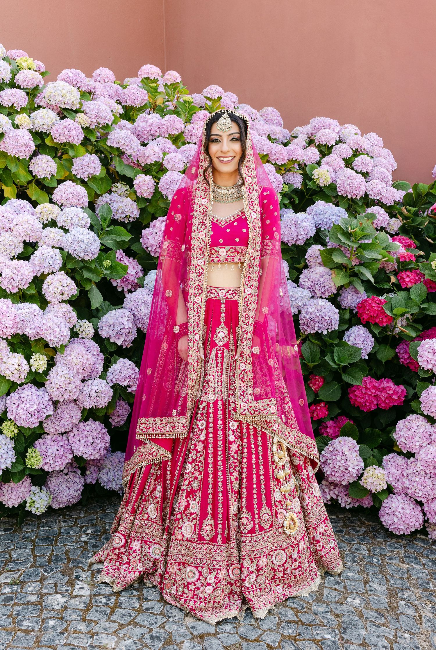Stunning bridal portraits against a backdrop of pink and purple hydrangeas featuring a red embroidered lehenga.
