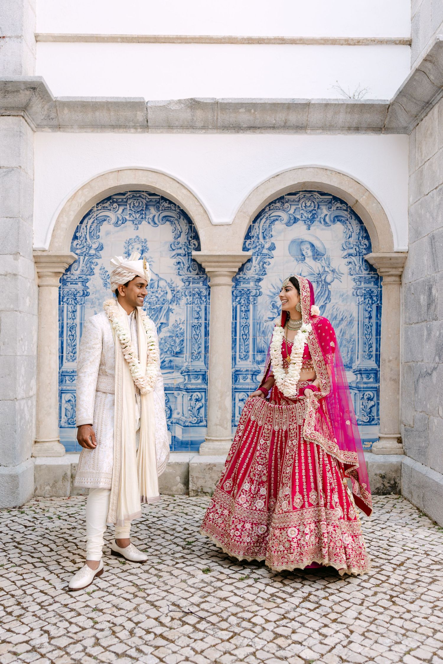 Wedding couple poses against blue and white tiled wall in traditional cultural attire.