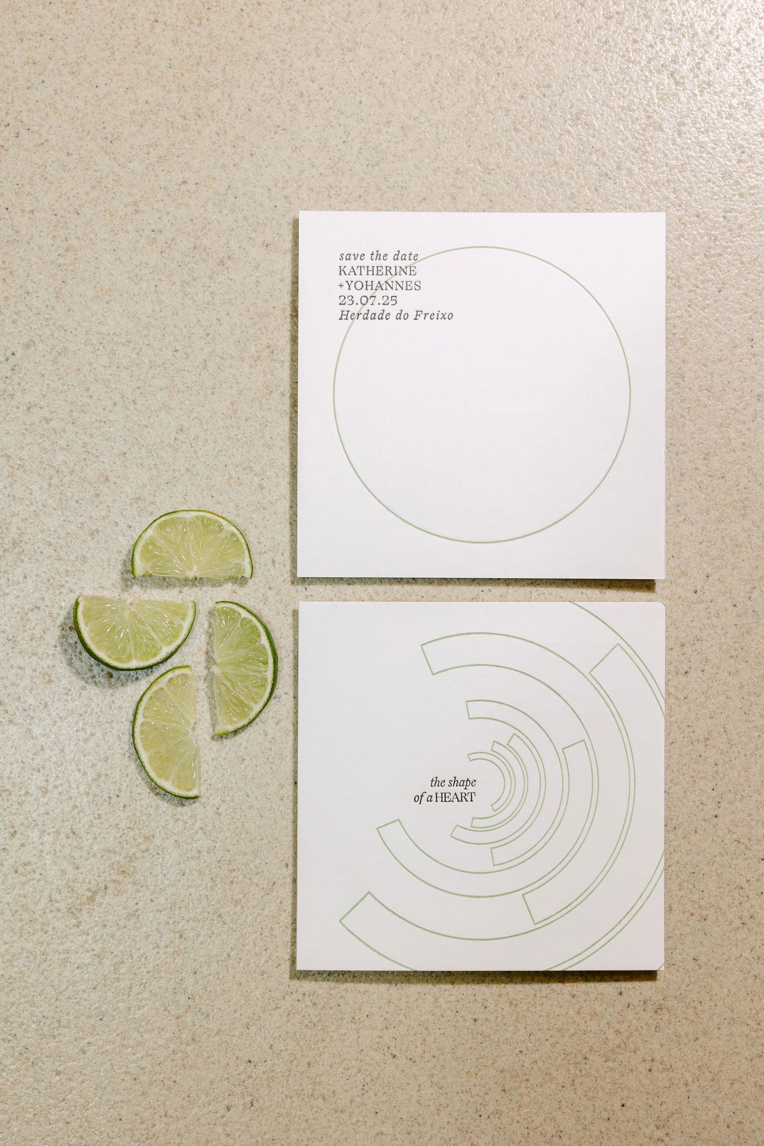 Two minimalist white save-the-date cards with geometric circle designs beside fresh lime slices on a beige surface.