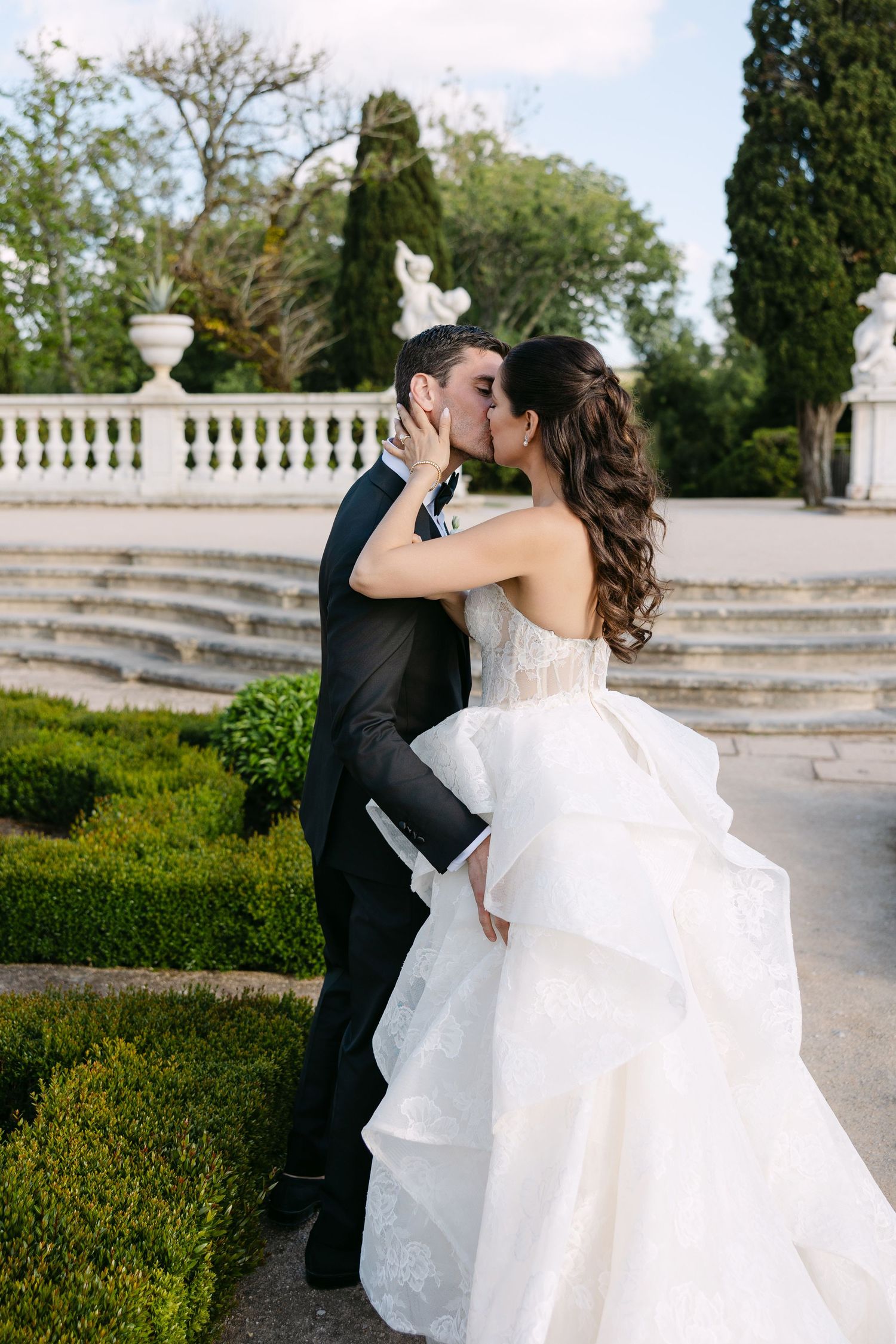 Bride and groom sharing a romantic kiss in a formal garden with stone balustrade backdrop.