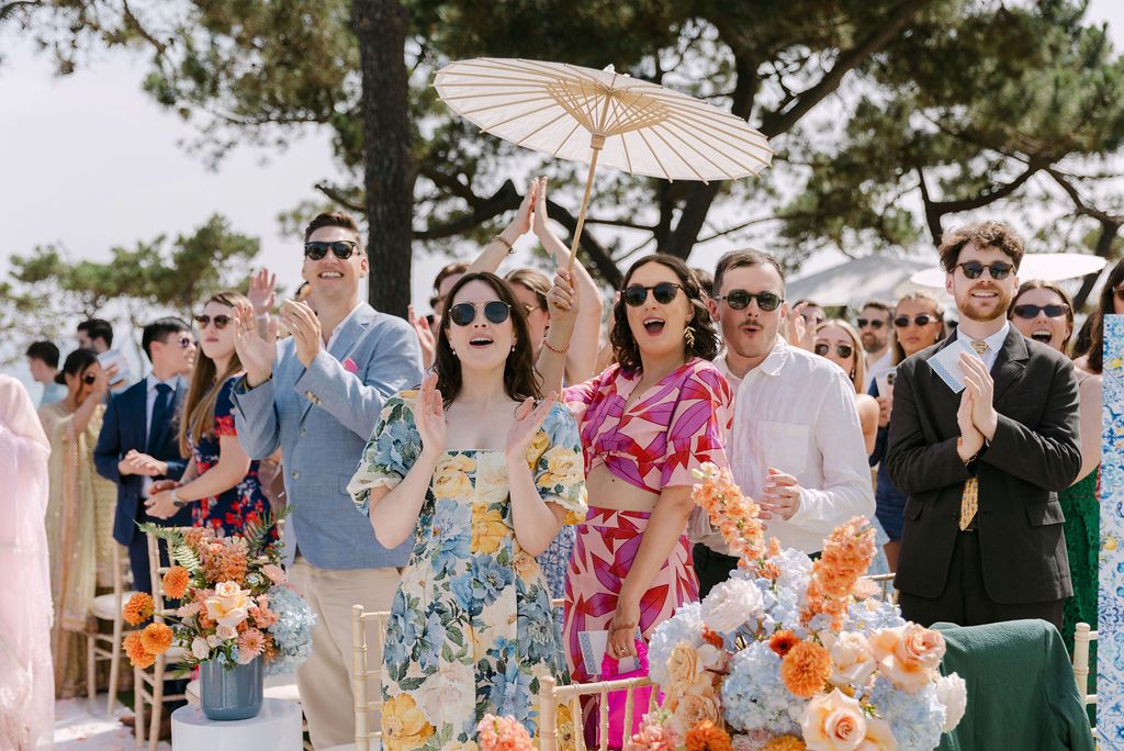 Wedding guests in pastel attire celebrating with parasols at an outdoor reception.