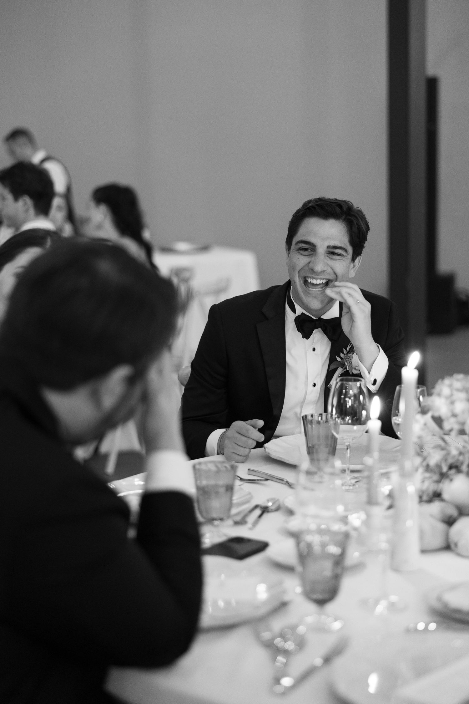 Elegant black and white photo of a formal dinner reception with guests seated at a candlelit table.