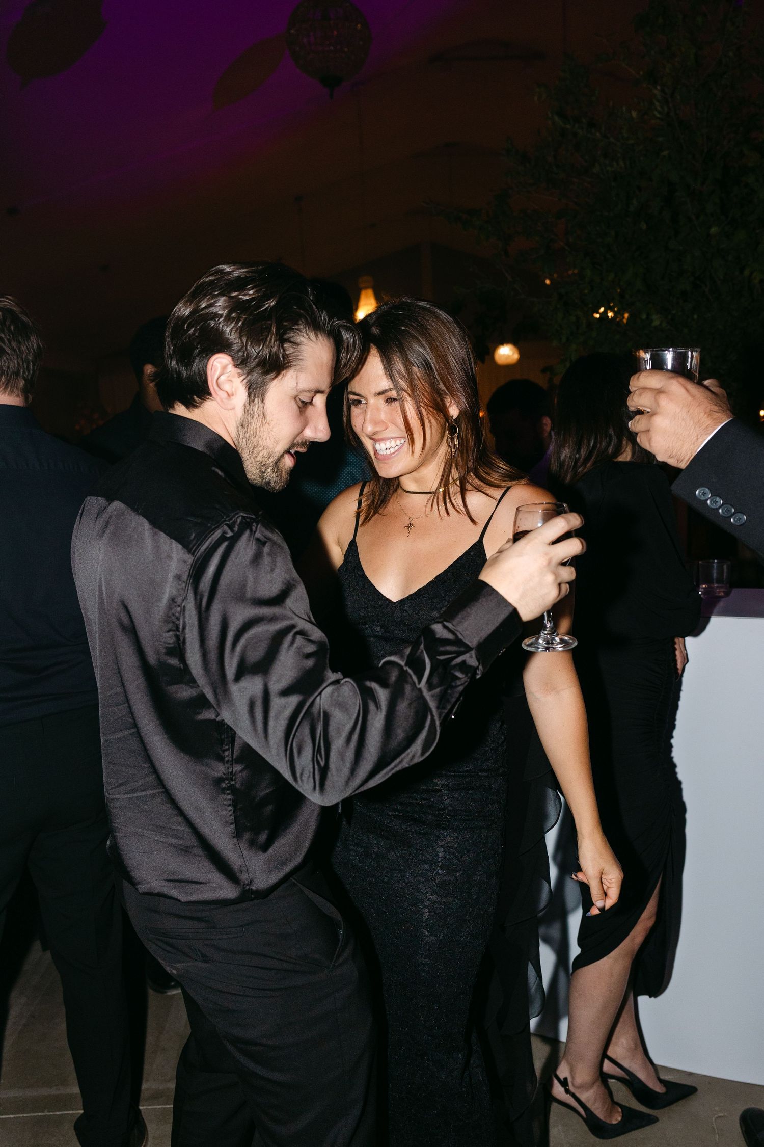 Couples dancing and enjoying themselves at a dimly lit party with purple ambient lighting.