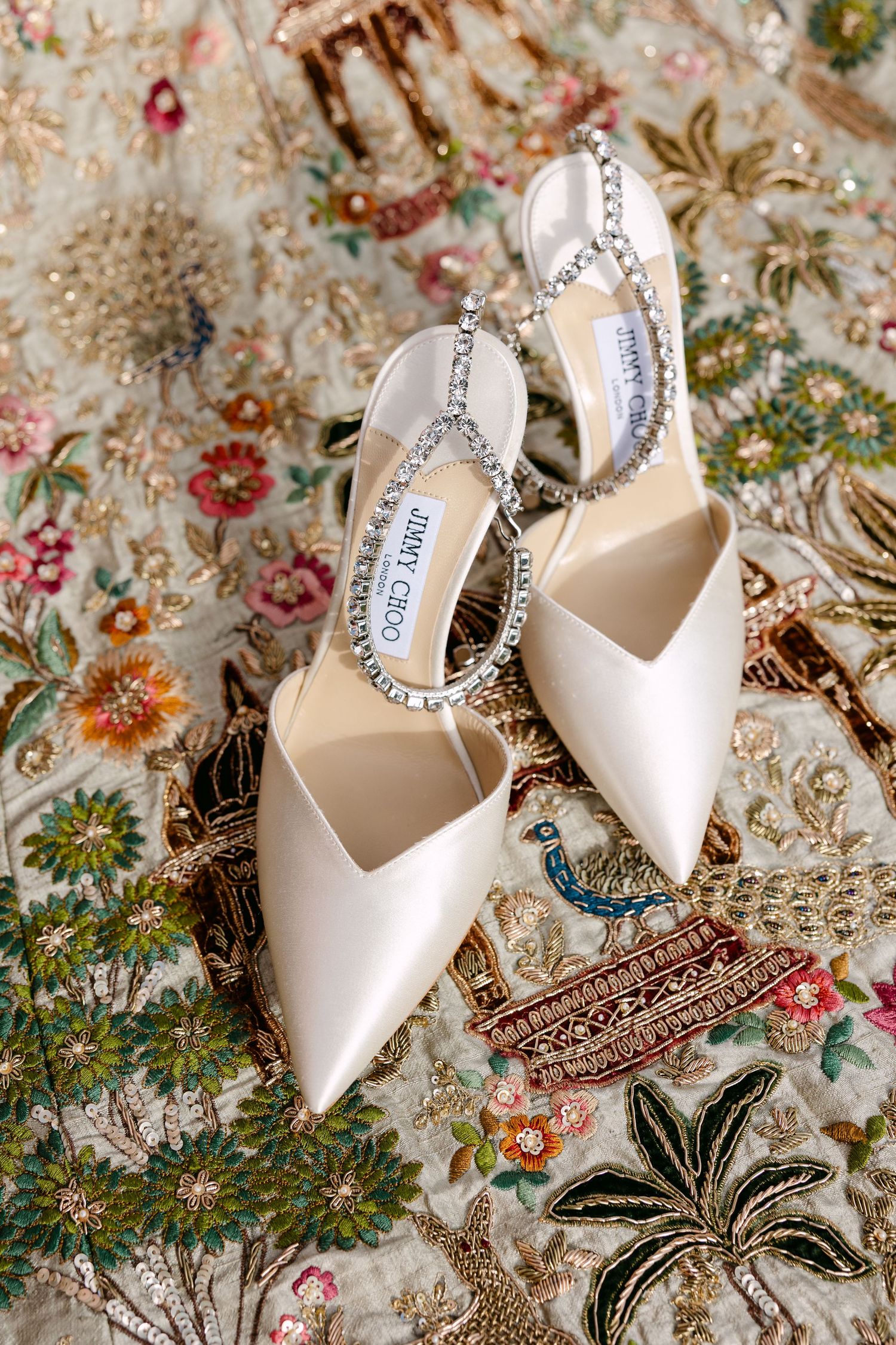 White bridal shoes with crystal details displayed on an ornate floral patterned fabric.