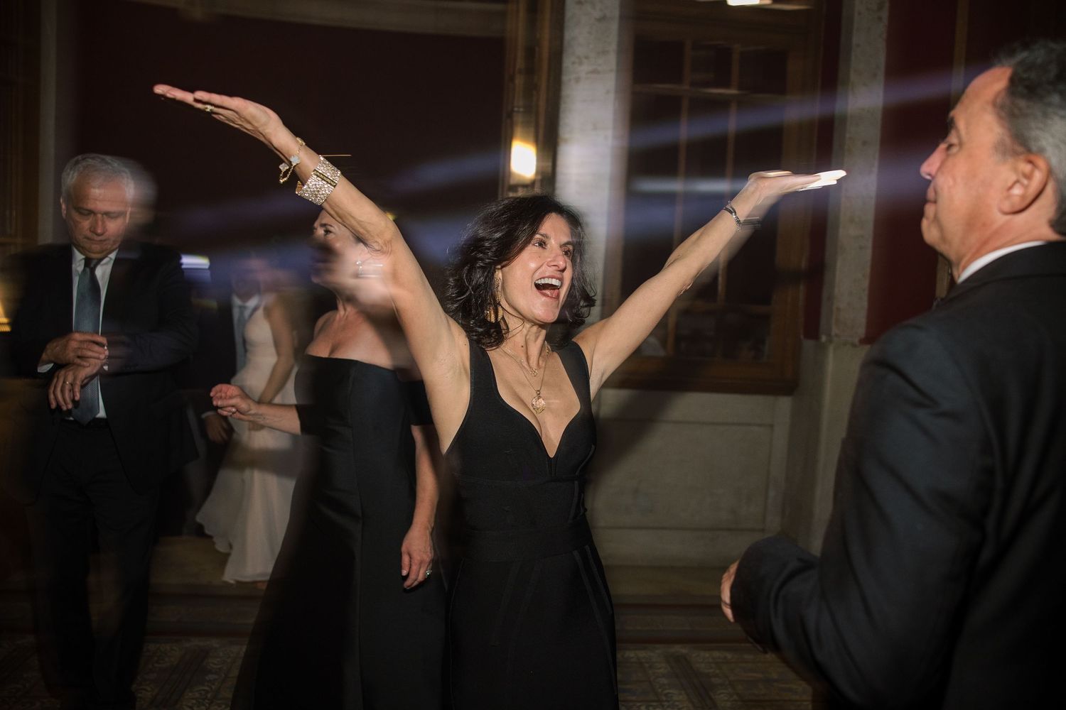 Wedding guests dancing and celebrating with raised arms at indoor reception.