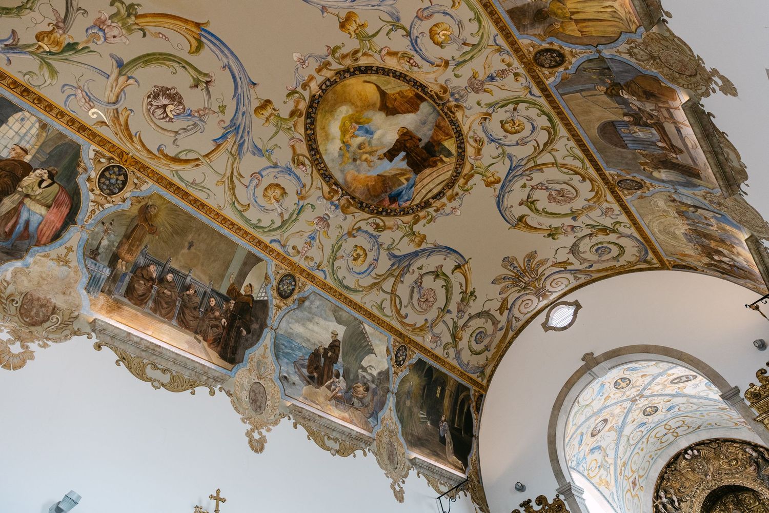 Ornate baroque ceiling with gilded decorations and religious frescoes in a historic church.