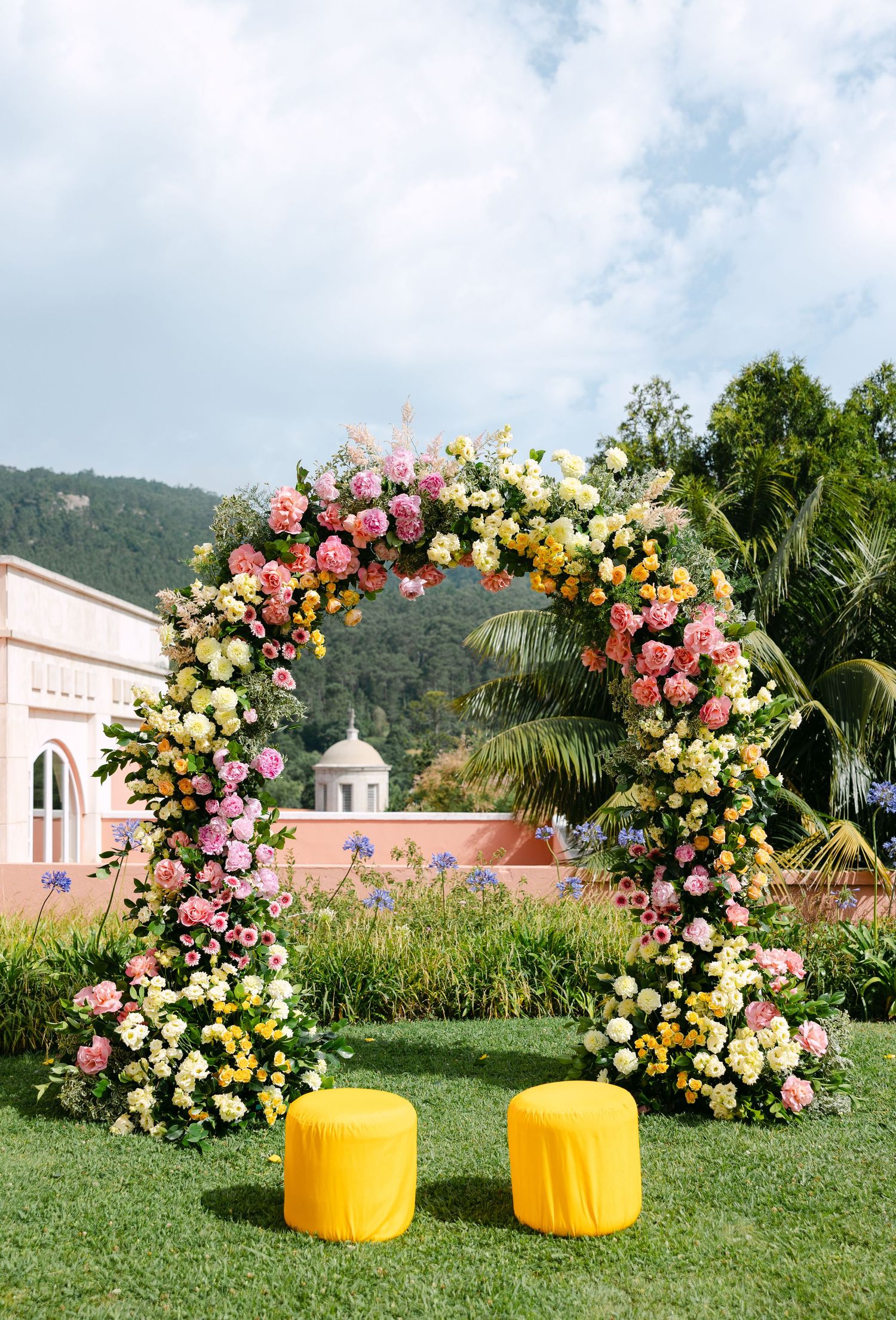 Floral arch with pink and yellow roses decorating an outdoor garden space with yellow accent pieces.