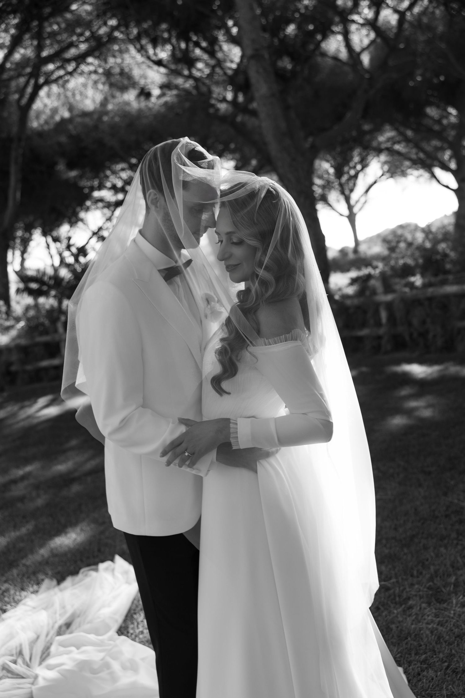 Intimate black and white portrait of newlyweds embracing in a wooded setting.