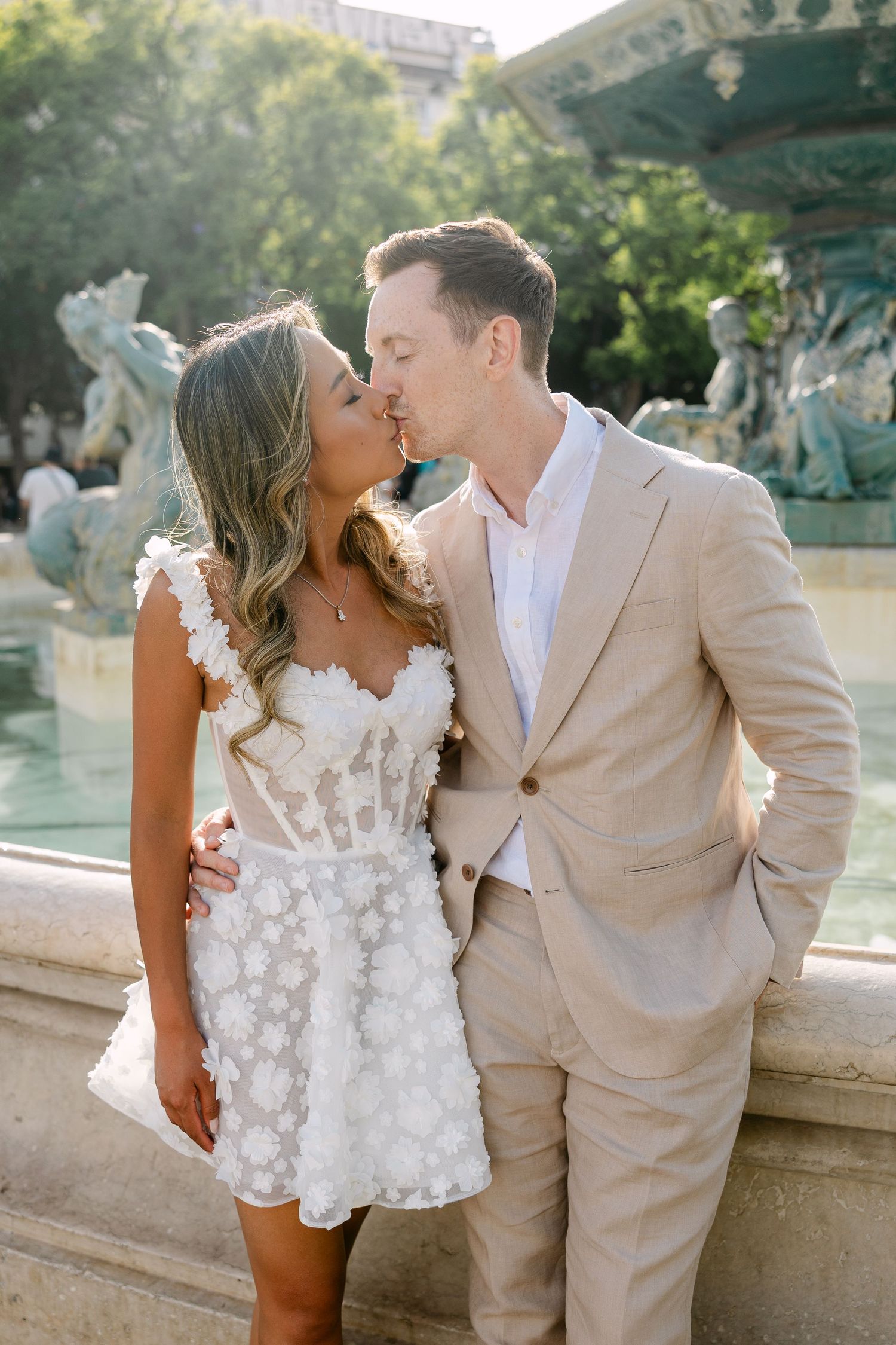 Romantic couple shares intimate moments by a fountain in formal attire.