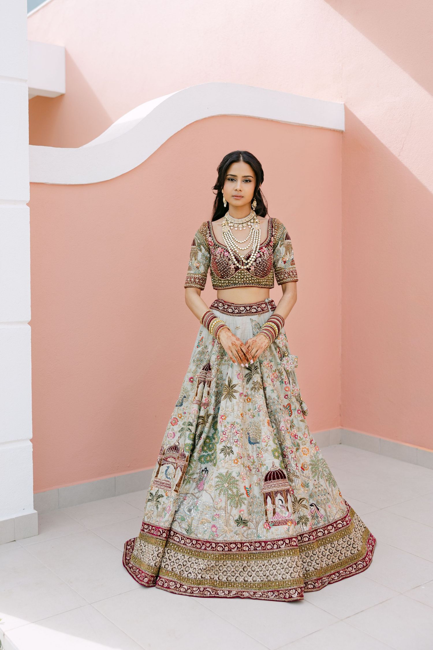 Elegant floral lehenga with intricate embroidery and traditional Indian bridal wear against a pink wall backdrop.