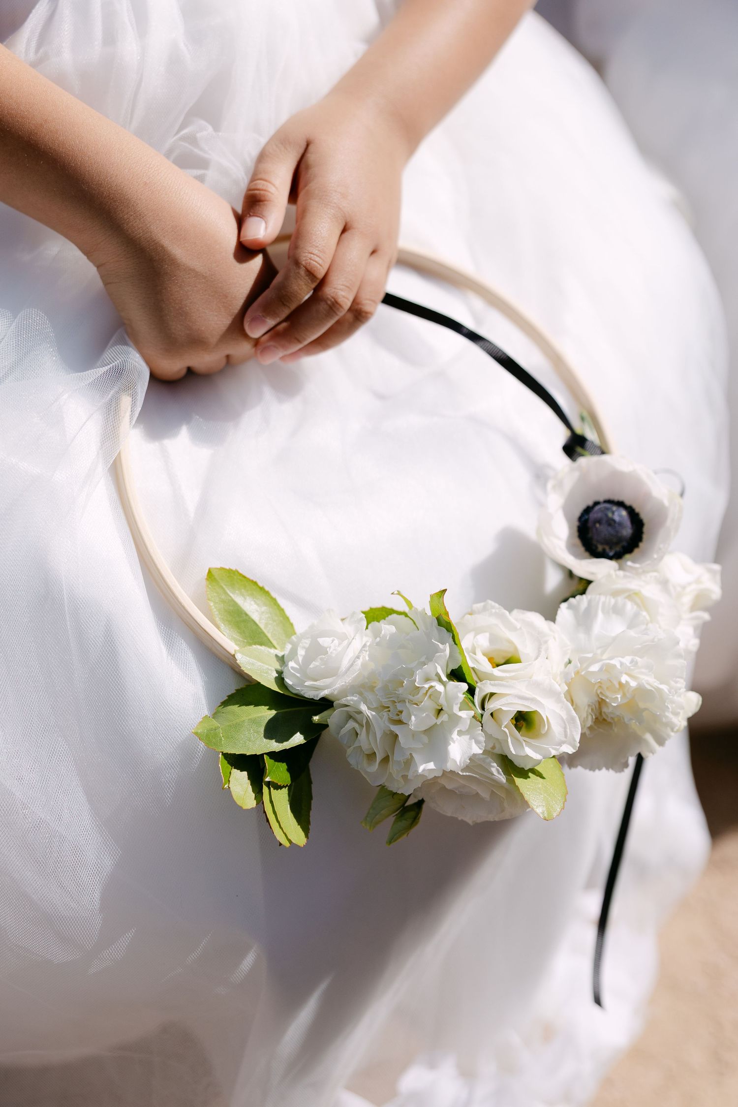 Bride in white dress holding a circular hoop bouquet adorned with white roses and anemone flowers.