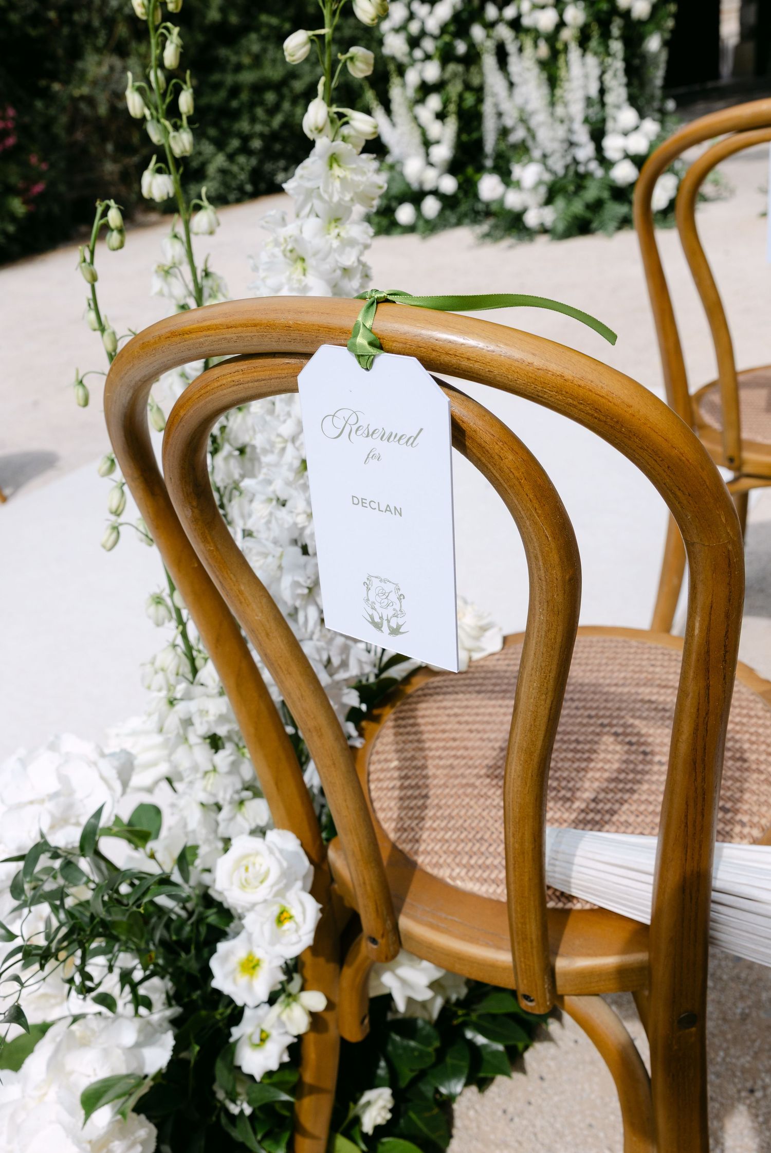 Elegant wooden chairs decorated with white floral arrangements and name cards for a wedding ceremony.